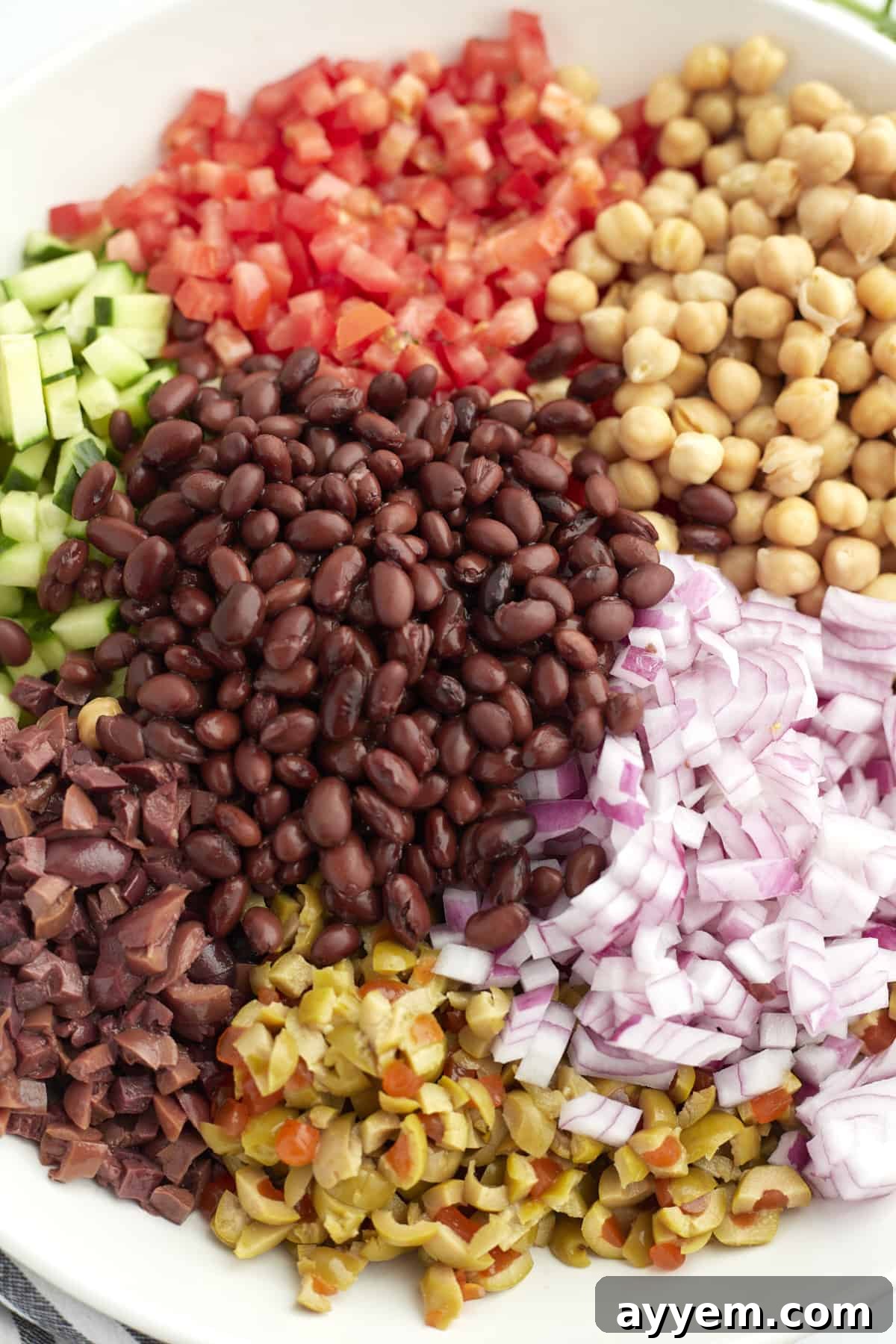 chopped tomatoes, chickpeas, red onion, corn, black beans, olives, and cucumbers in a bowl.