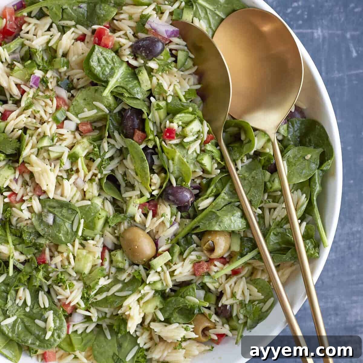 A beautifully presented bowl of Greek orzo pasta salad, vibrant with fresh vegetables and a creamy dressing.