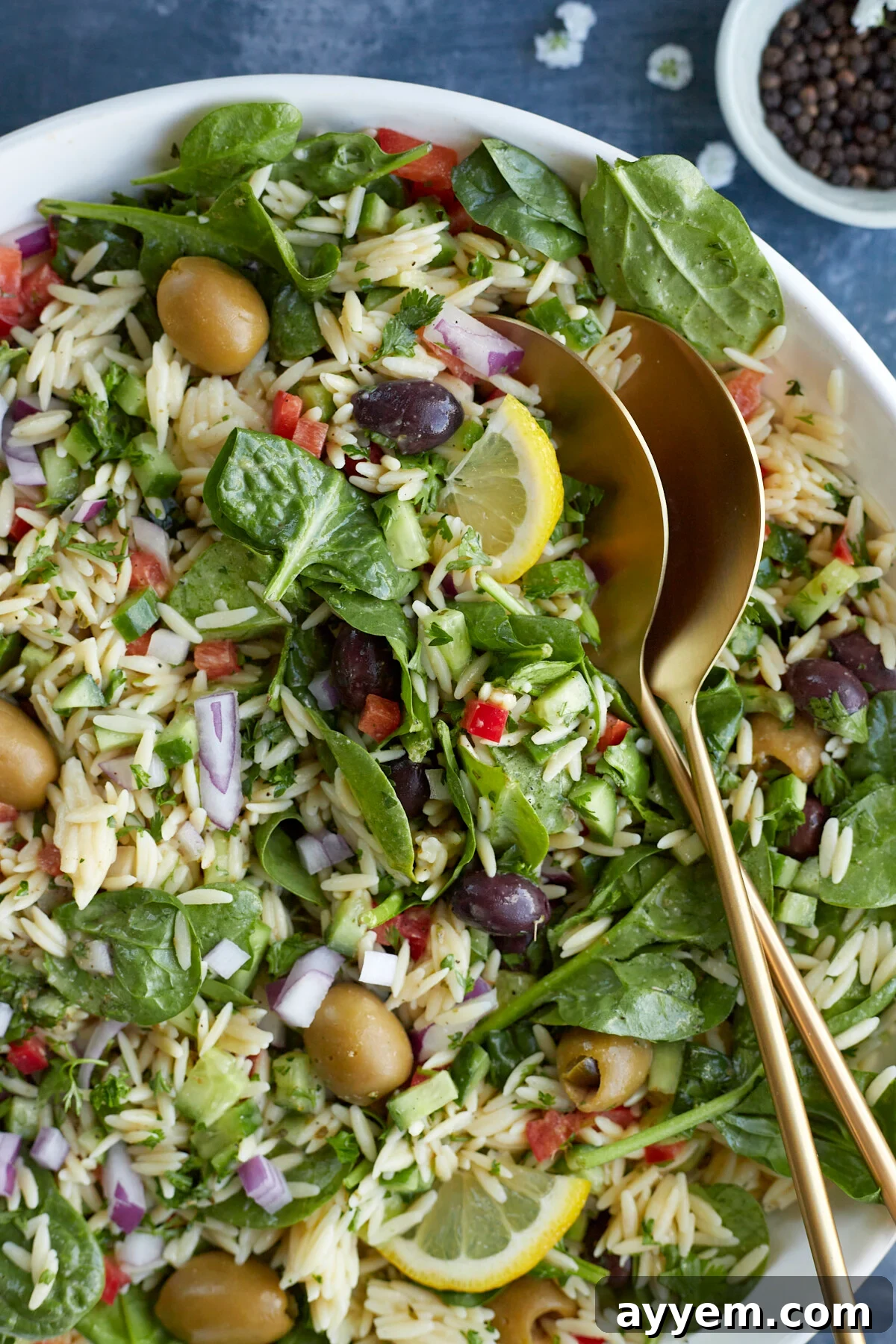 A large bowl of Greek orzo pasta salad, garnished with fresh herbs and serving spoons, ready to be enjoyed.