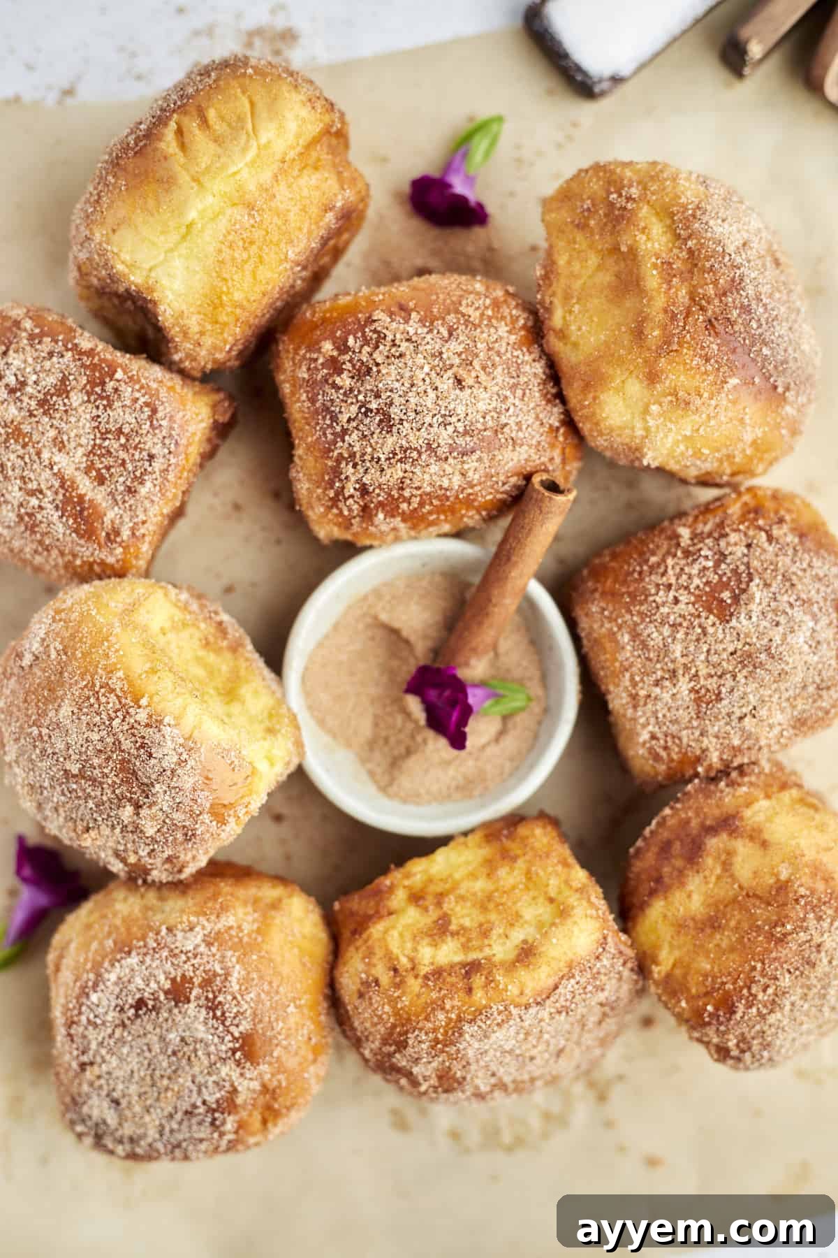 cinnamon bun air fryer french toast buns on a piece of parchment paper with a bowl of cinnamon sugar in the center