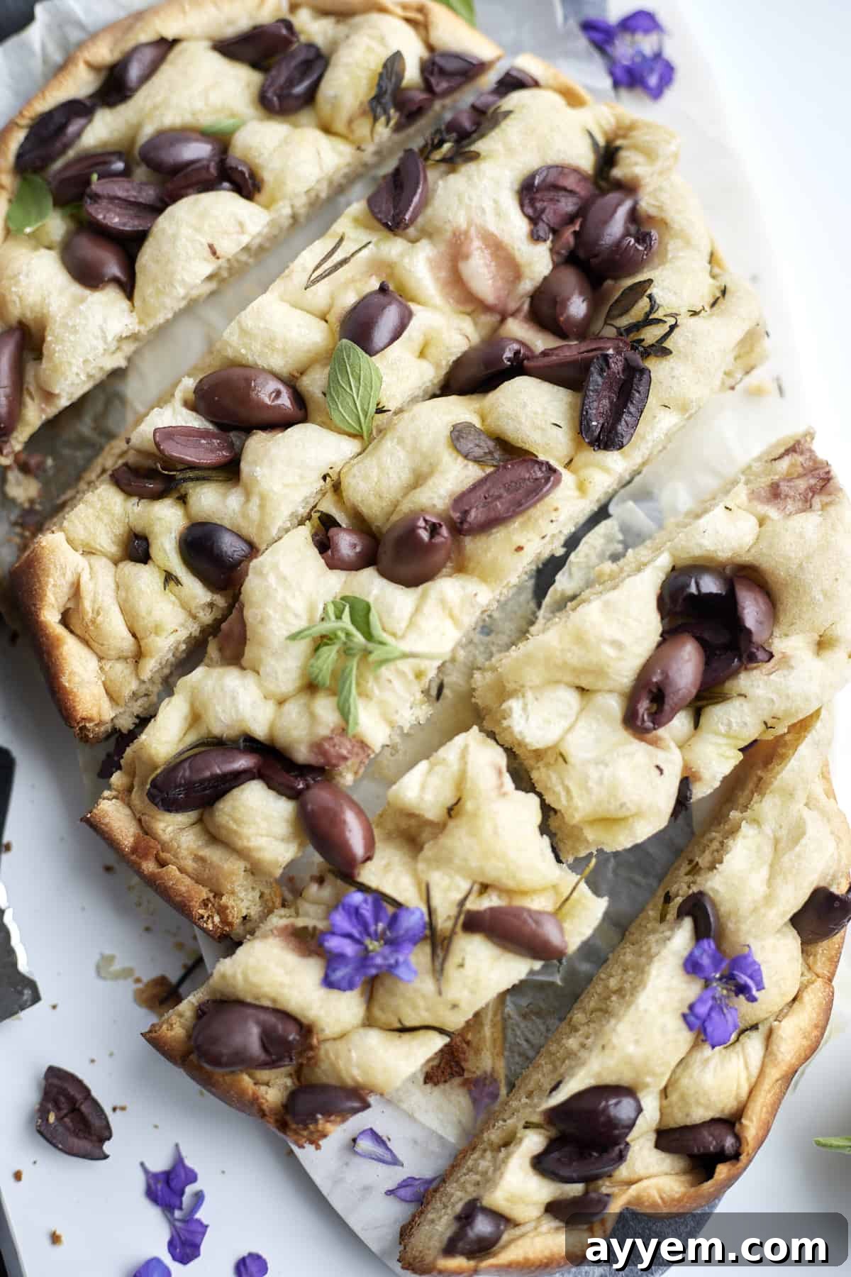 focaccia bread with kalamata olives on a marble slab garnished with fresh basil, showcasing a golden crust and dimpled surface