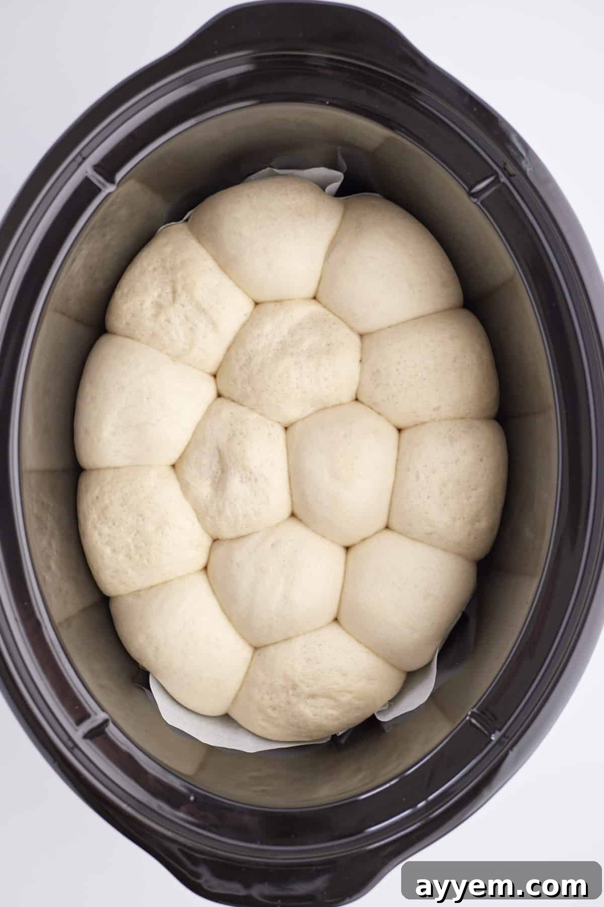 overhead image of partially baked dinner rolls in the bottom of a slow cooker, showing they have risen significantly