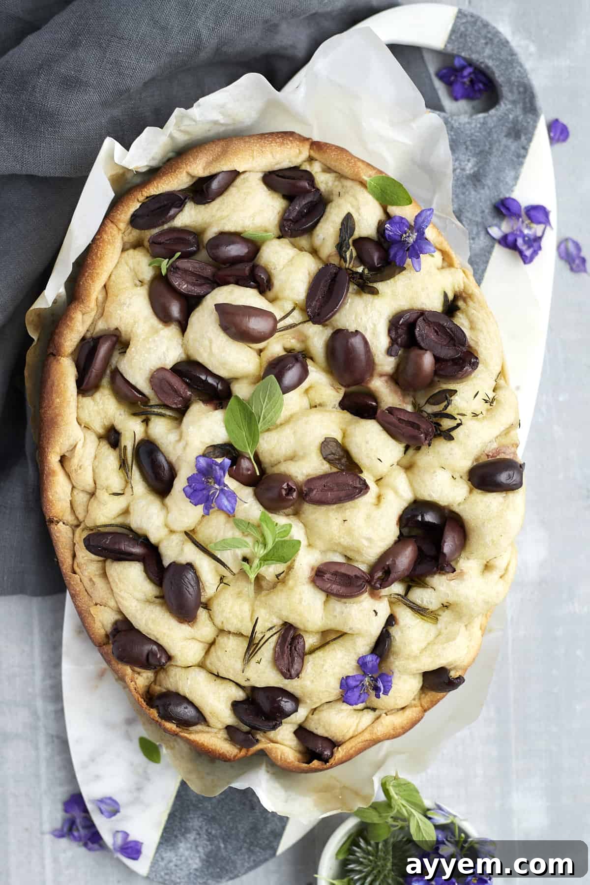 focaccia bread with kalamata olives on a marble slab garnished with fresh basil, ready to be sliced and served