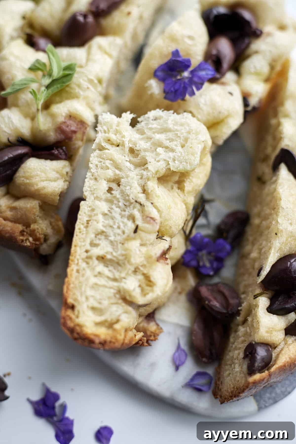 closeup of focaccia bread with kalamata olives on a marble slab garnished with fresh basil, highlighting the texture and toppings