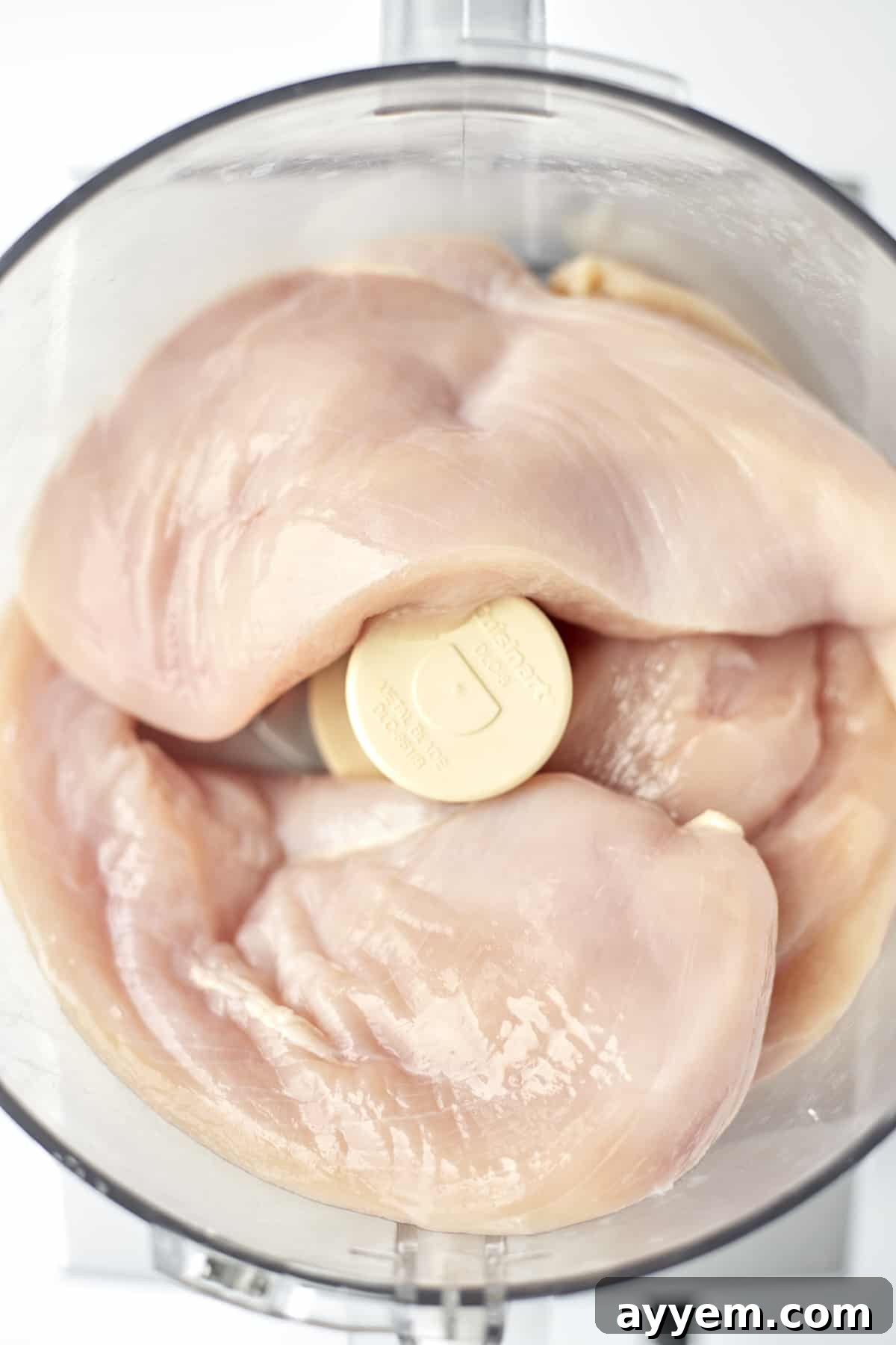 Overhead shot of raw chicken breasts in a food processor, ready to be pulsed into ground chicken.