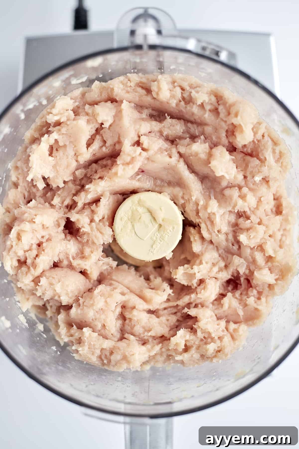 Close-up of finely pulsed ground chicken in a food processor, ready for cooking.