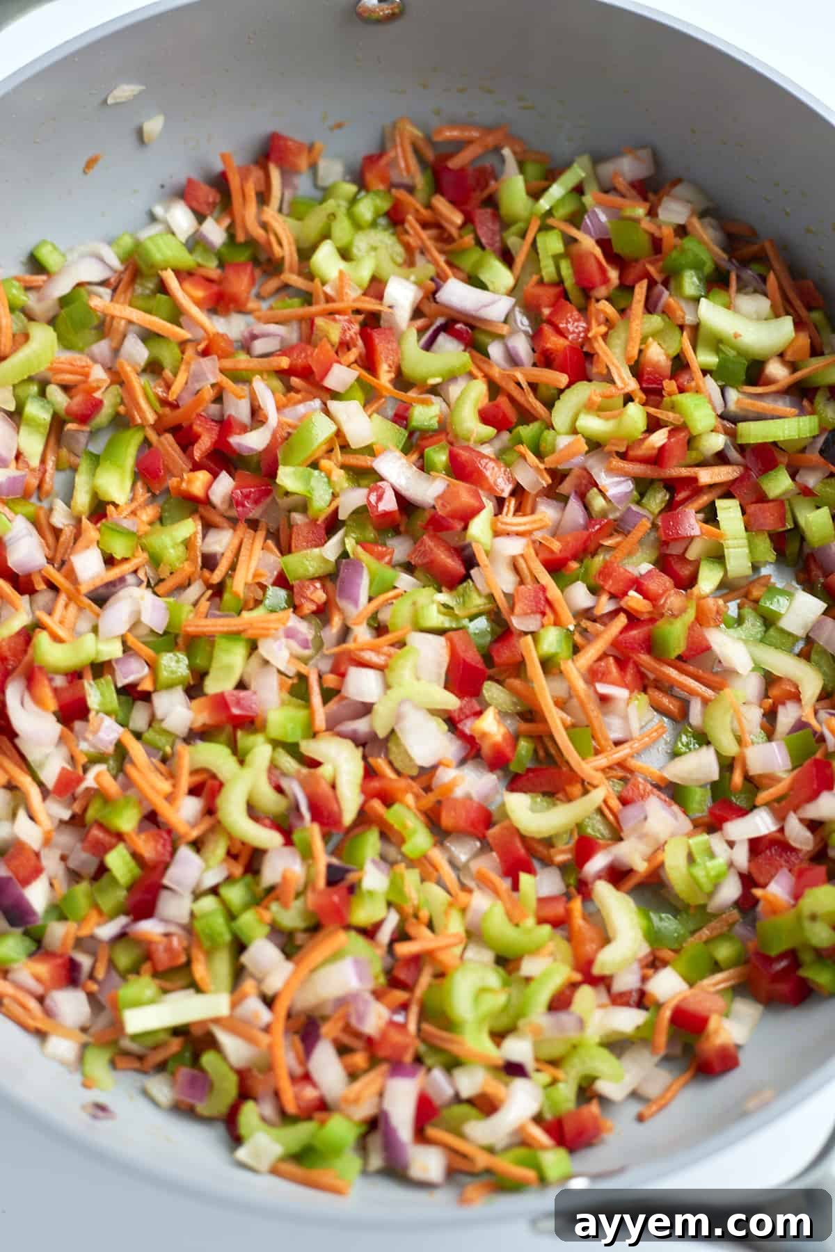 A colorful medley of diced vegetables (carrots, celery, bell peppers, red onion) sizzling in a skillet.