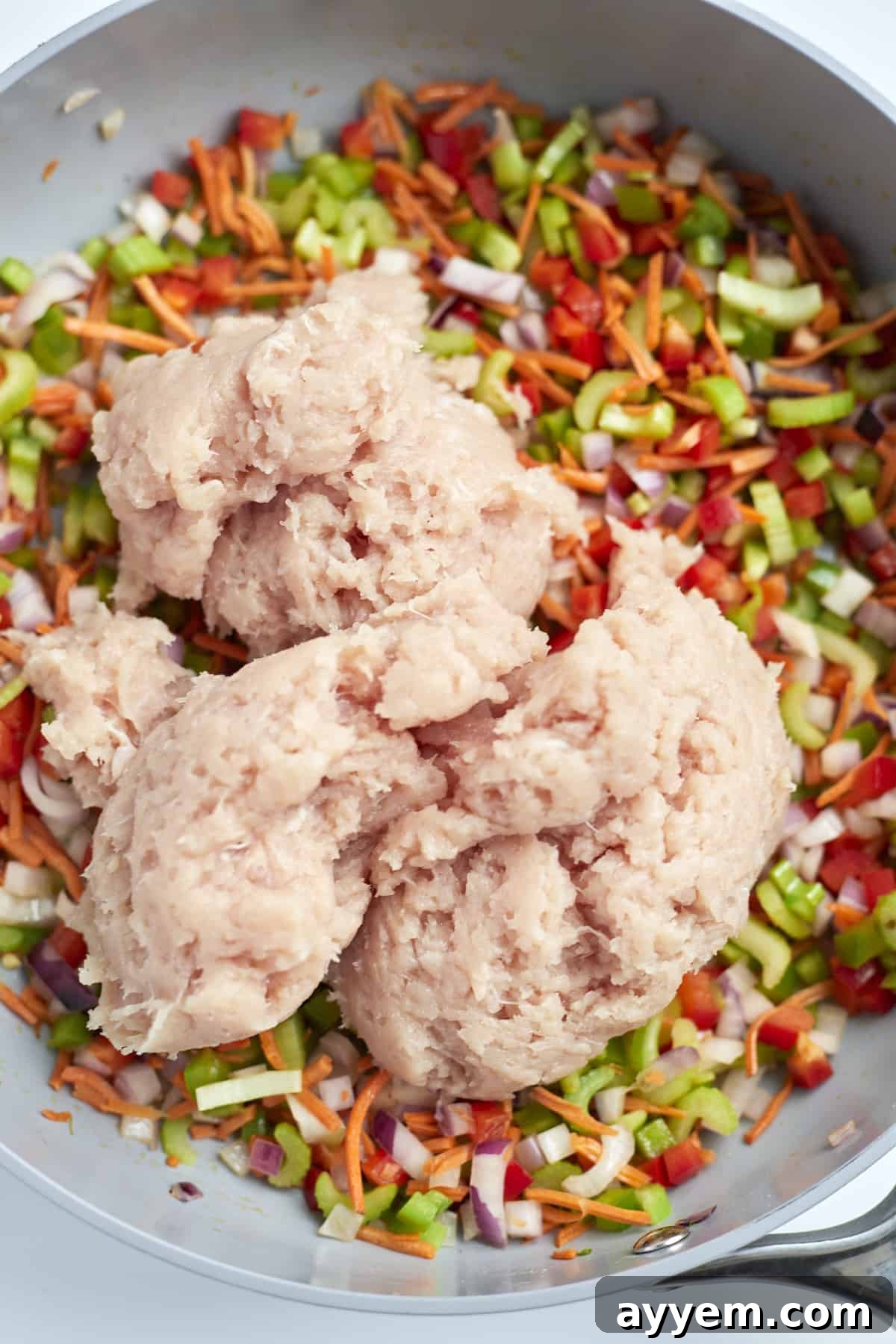 Uncooked ground chicken added on top of the sautéed vegetables in a large skillet, ready to be stirred.