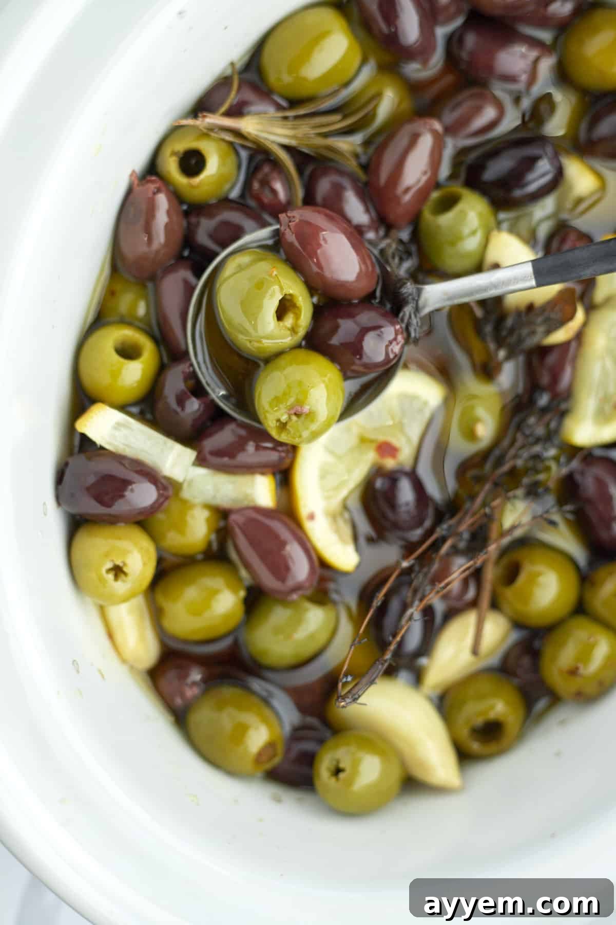 roasted olives being lifted out of a slow cooker with a spoon