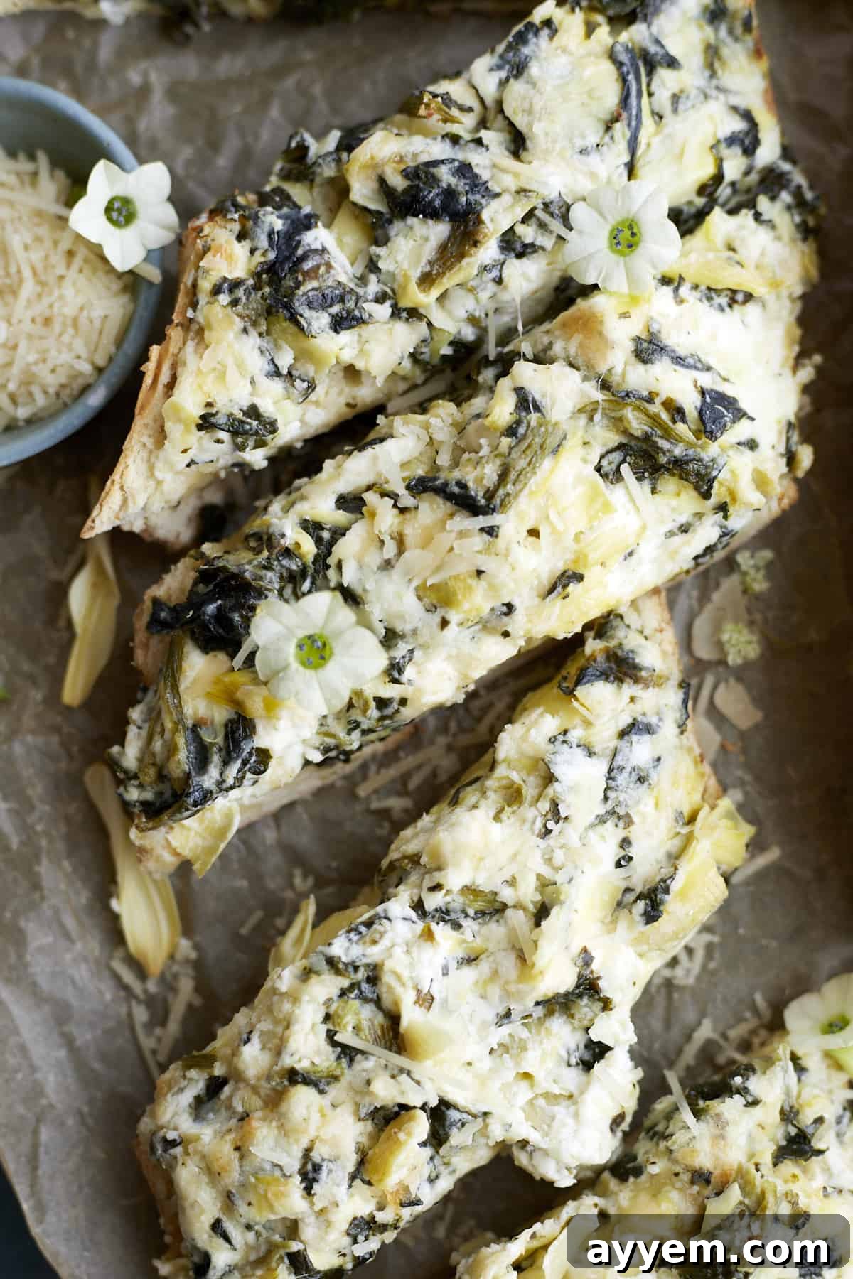 Loaded Garlic Bread with Spinach and Artichokes 2 Sliced pieces of golden-brown homemade garlic bread topped generously with a creamy spinach and artichoke mixture, fresh herbs visible.