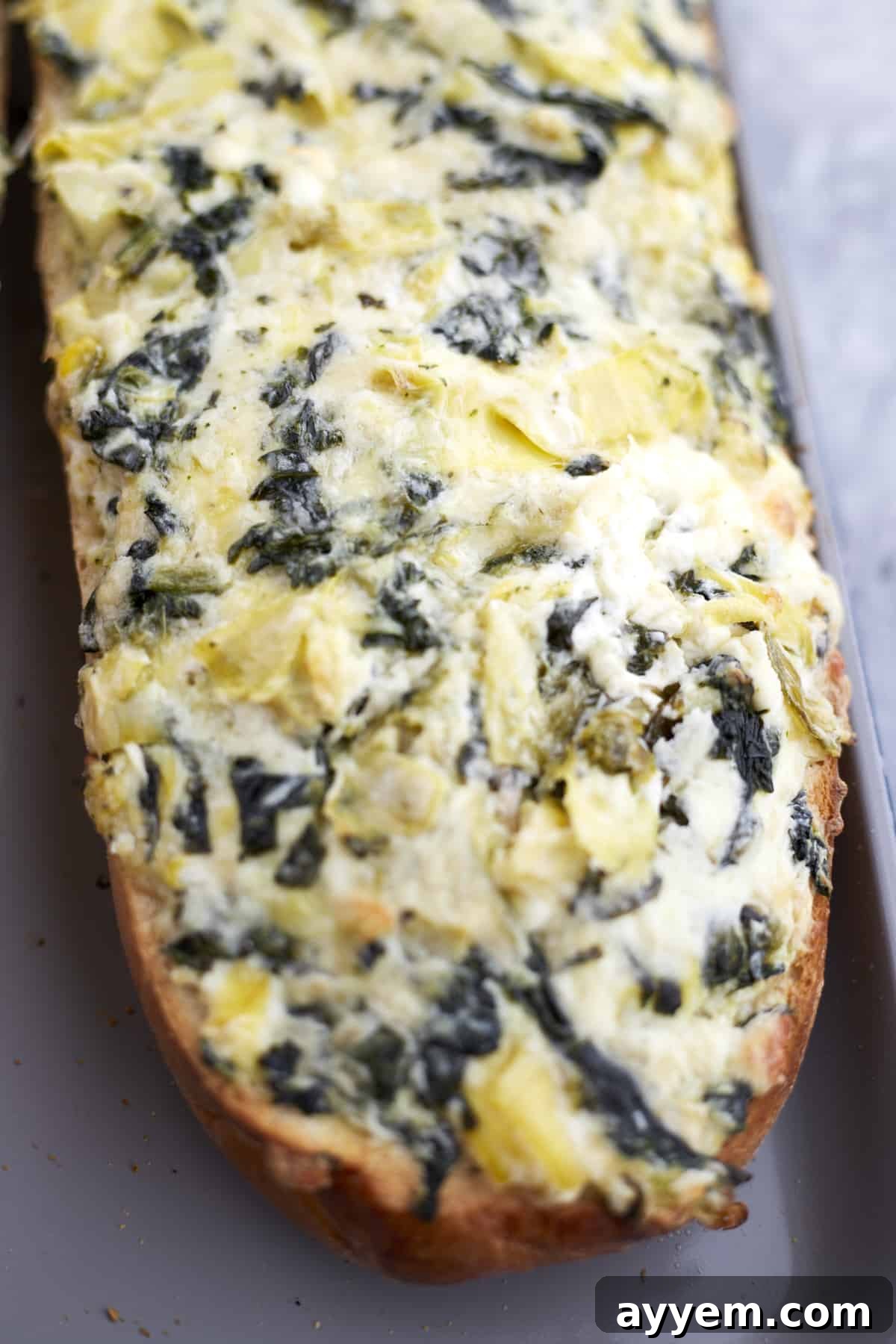 Loaded Garlic Bread with Spinach and Artichokes 5 A beautifully cooked loaf of homemade garlic bread with a bubbly, golden-brown spinach and artichoke dip topping, fresh out of the oven.