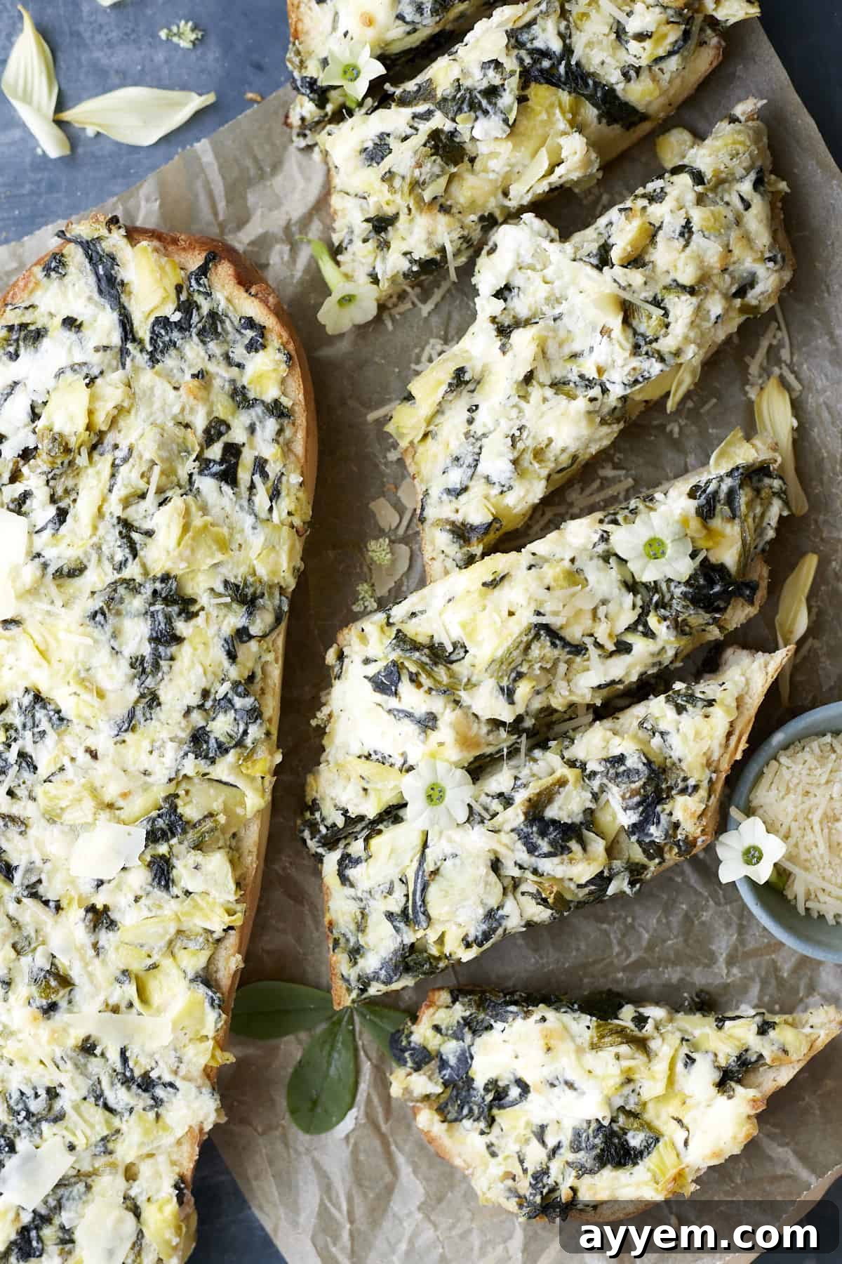 Loaded Garlic Bread with Spinach and Artichokes 6 A whole loaf of homemade garlic bread with spinach and artichokes next to several neatly sliced pieces of the same garlic bread, showcasing the golden crust and creamy topping.