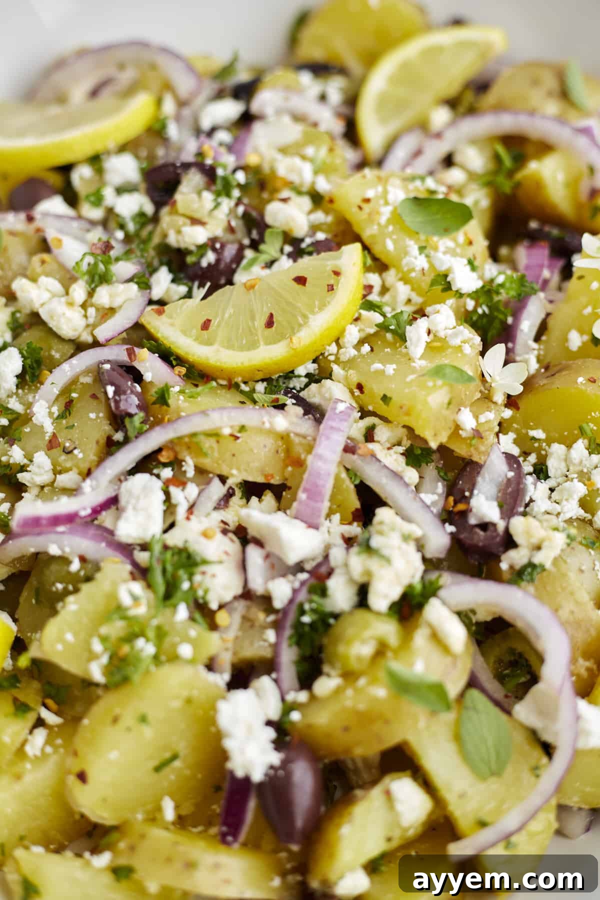 Close-up of vibrant Lemon Greek Roasted Potatoes garnished with fresh feta, thinly sliced red onion, and bright lemon wedges