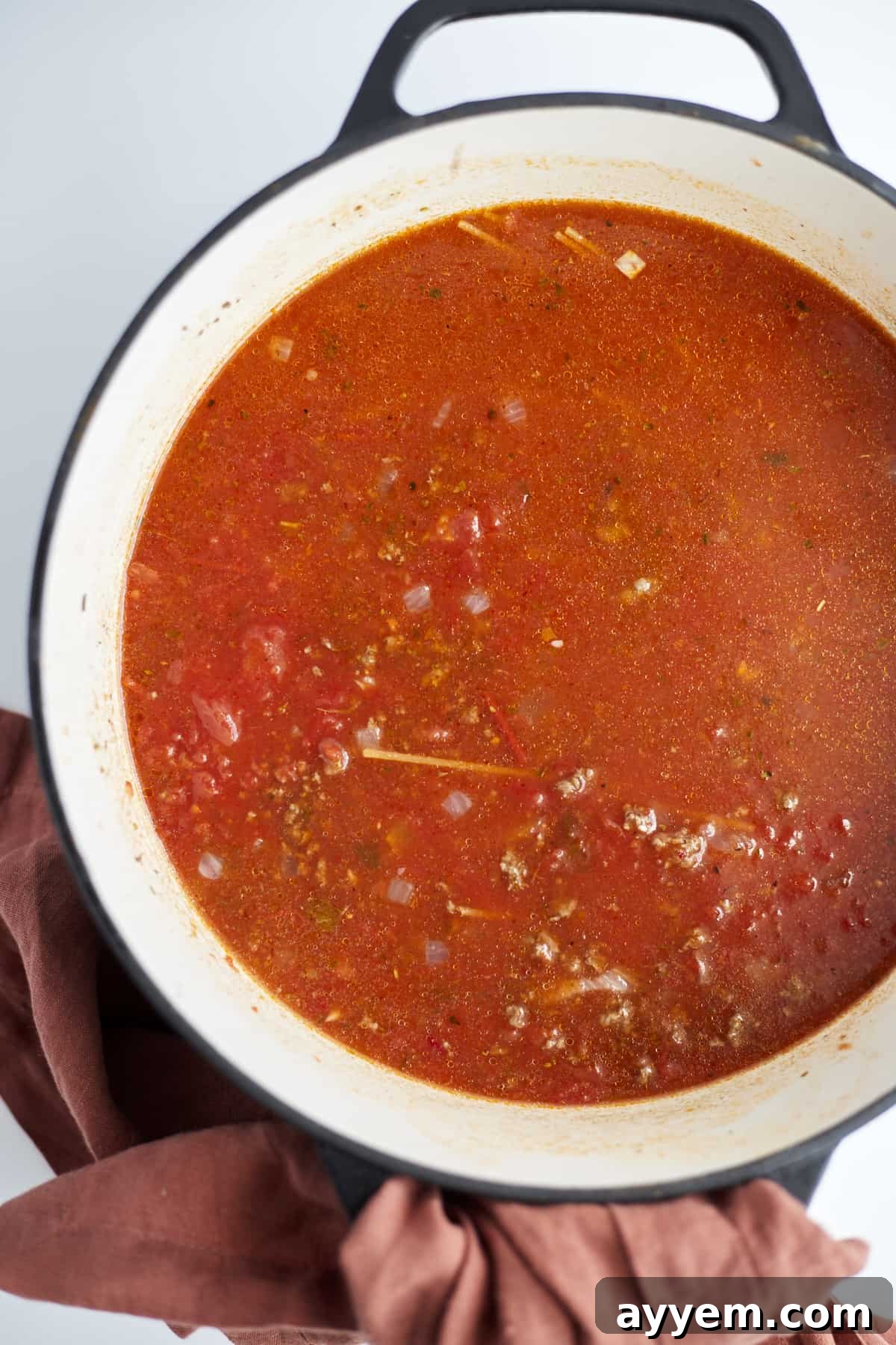 Overhead image of a large pot filled with browned beef, sautéed onions, and rich tomato sauce, simmering to create the perfect one-pot spaghetti.