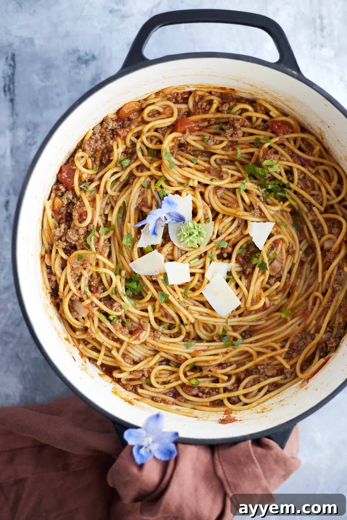 Overhead image of a large pot brimming with one-pot spaghetti and ground beef, beautifully garnished with fresh herbs and a generous sprinkle of shaved Parmesan cheese.