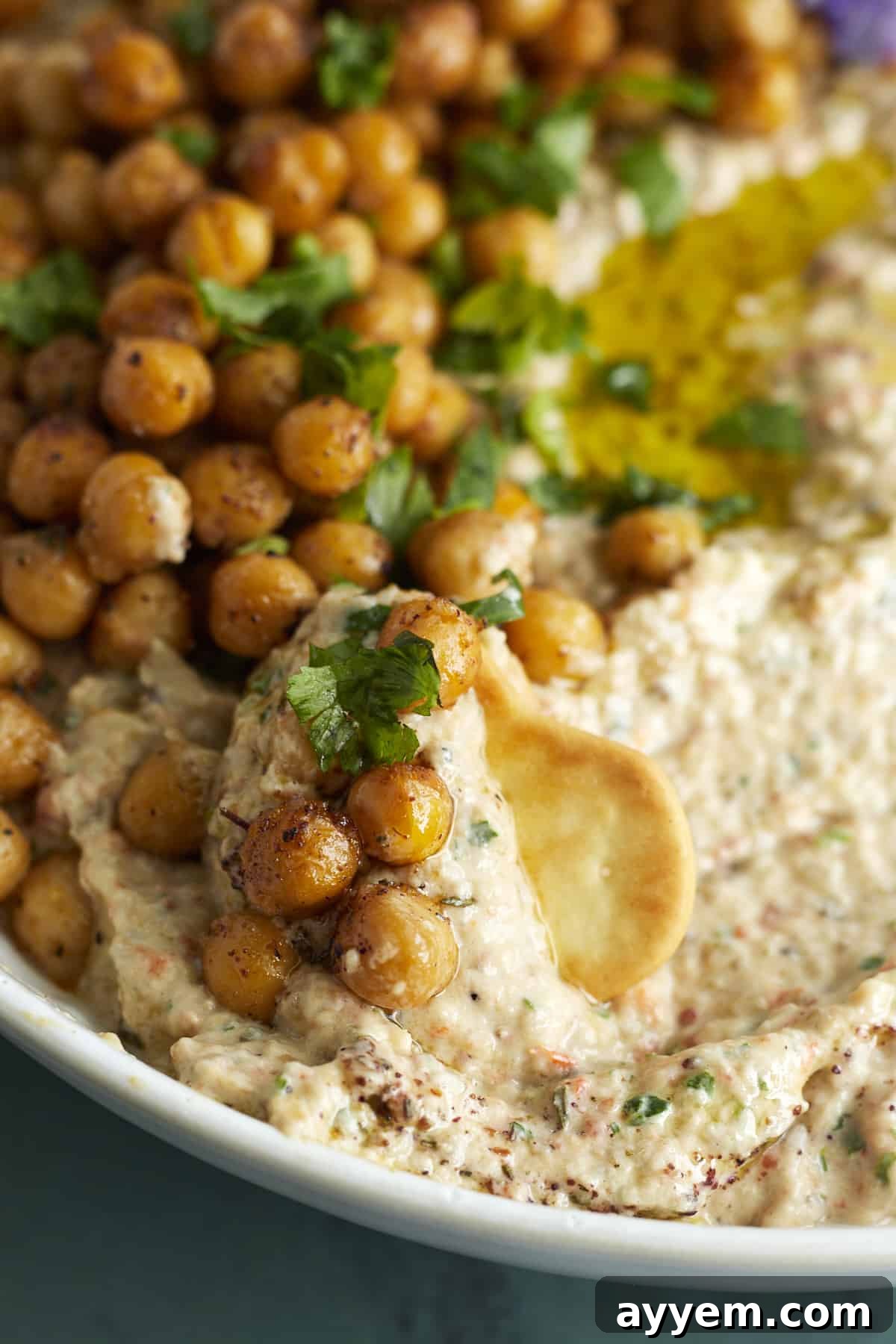 close up image of a cracker scooping up baba ganoush topped with crispy chickpeas