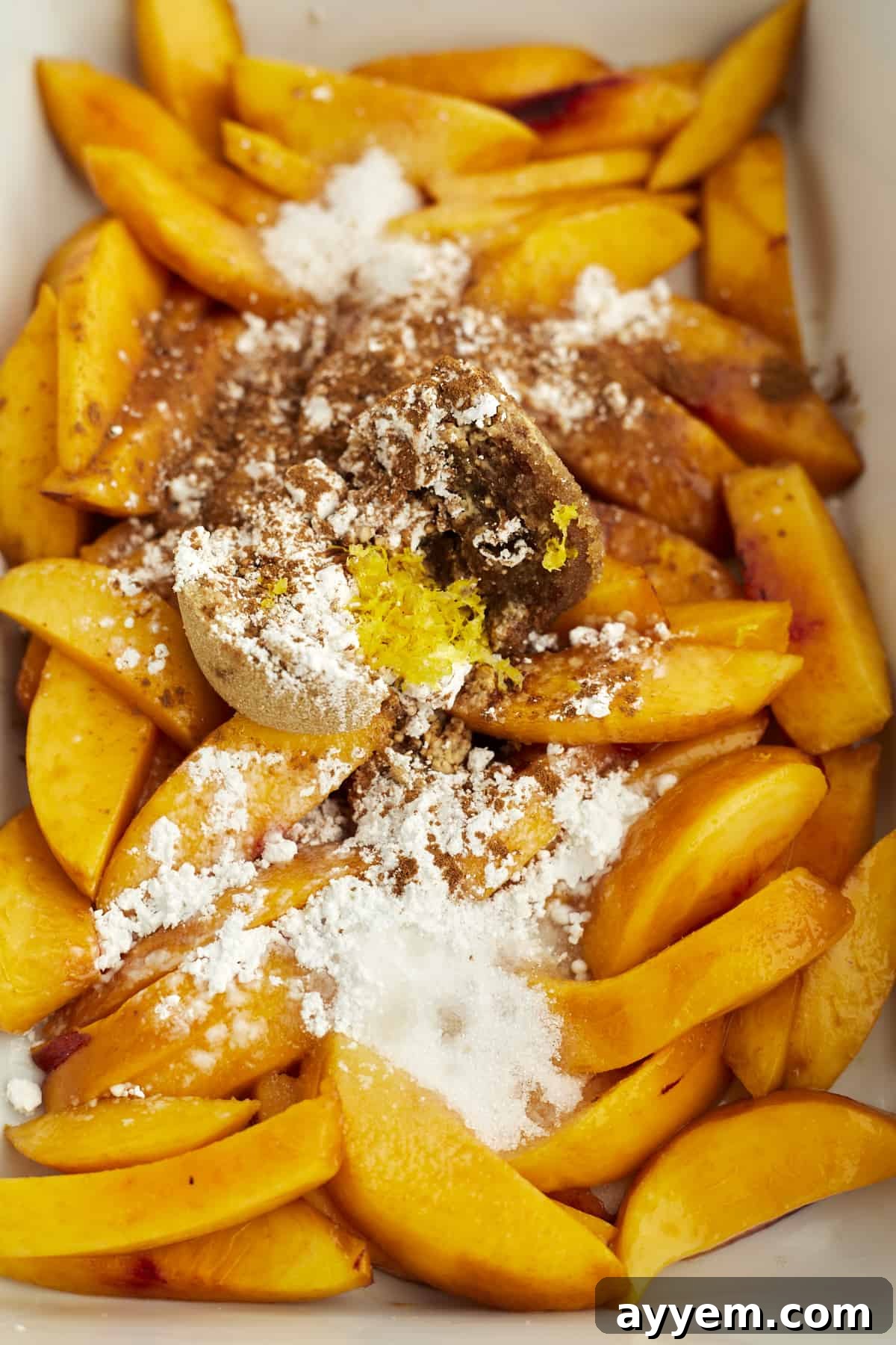 Delightfully Simple Peach Crisp 4 Close-up overhead image of perfectly sliced fresh peaches gently coated with a generous sprinkle of cinnamon and sugar, ready for baking.
