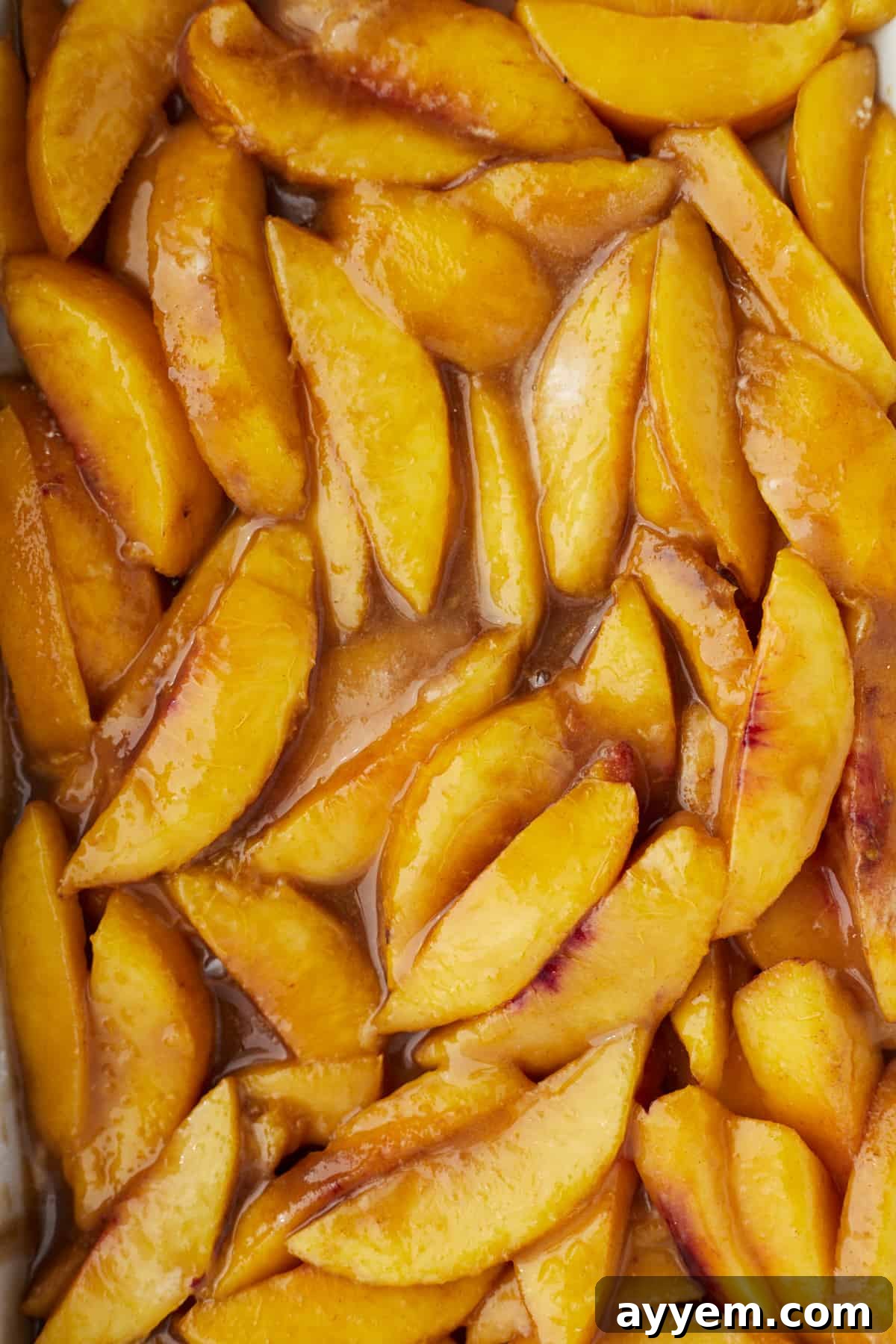 Delightfully Simple Peach Crisp 5 Detailed close-up image showing the glossy texture of ripe peach slices generously coated in a mixture of sugar and cinnamon, highlighting the spices clinging to the fruit.