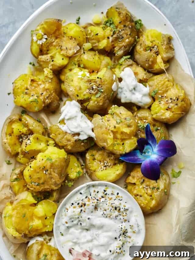 The Ultimate Crispy Smashed Potatoes 5 overehead image of smashed potatoes on a serving platter with a side of white creamy sauce.