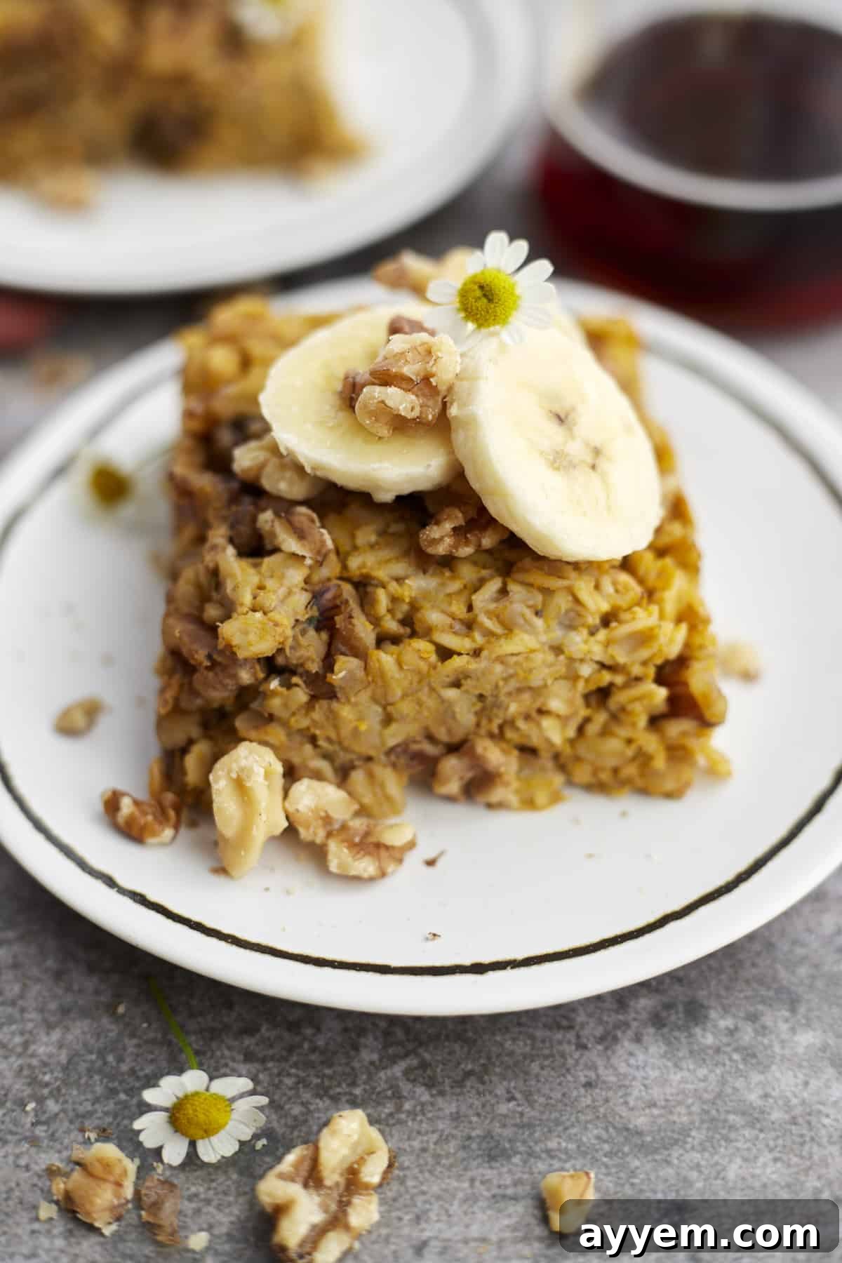 A white plate with a slice of baked pumpkin oatmeal topped with banana coins and walnuts, ready to be enjoyed.