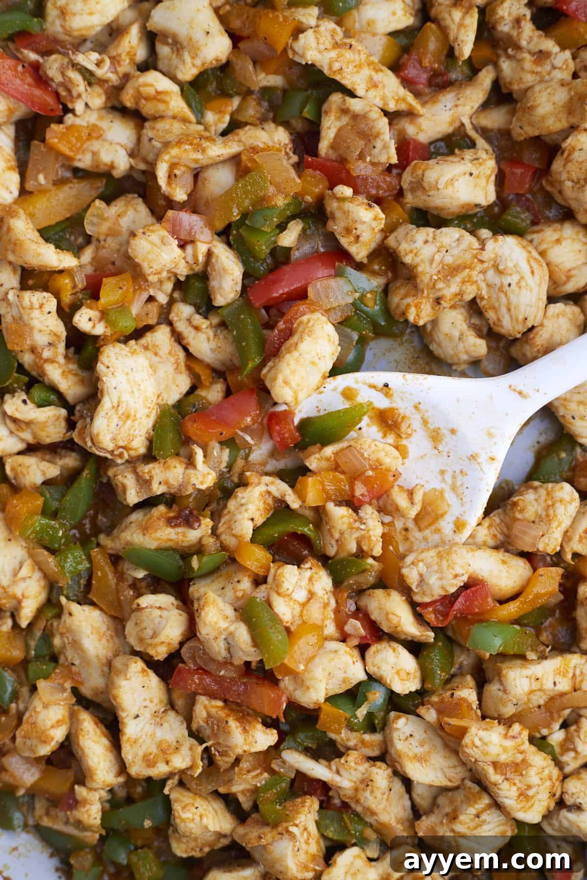 chicken fajita mixture with peppers and onions being stirred with a spoon