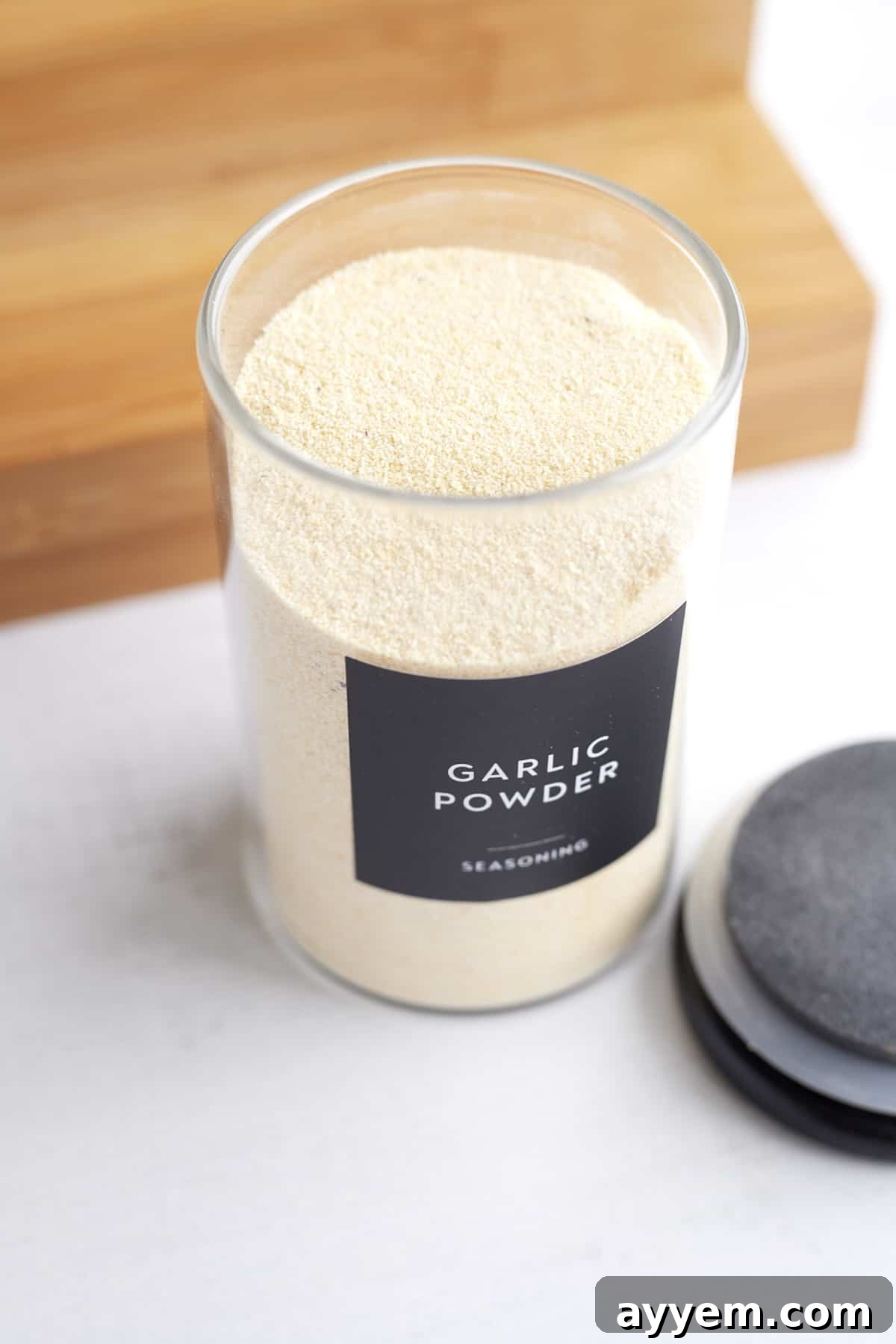 An overhead view of a clear spice container with a black lid and a black label indicating 'Garlic Powder', ready for organized storage.