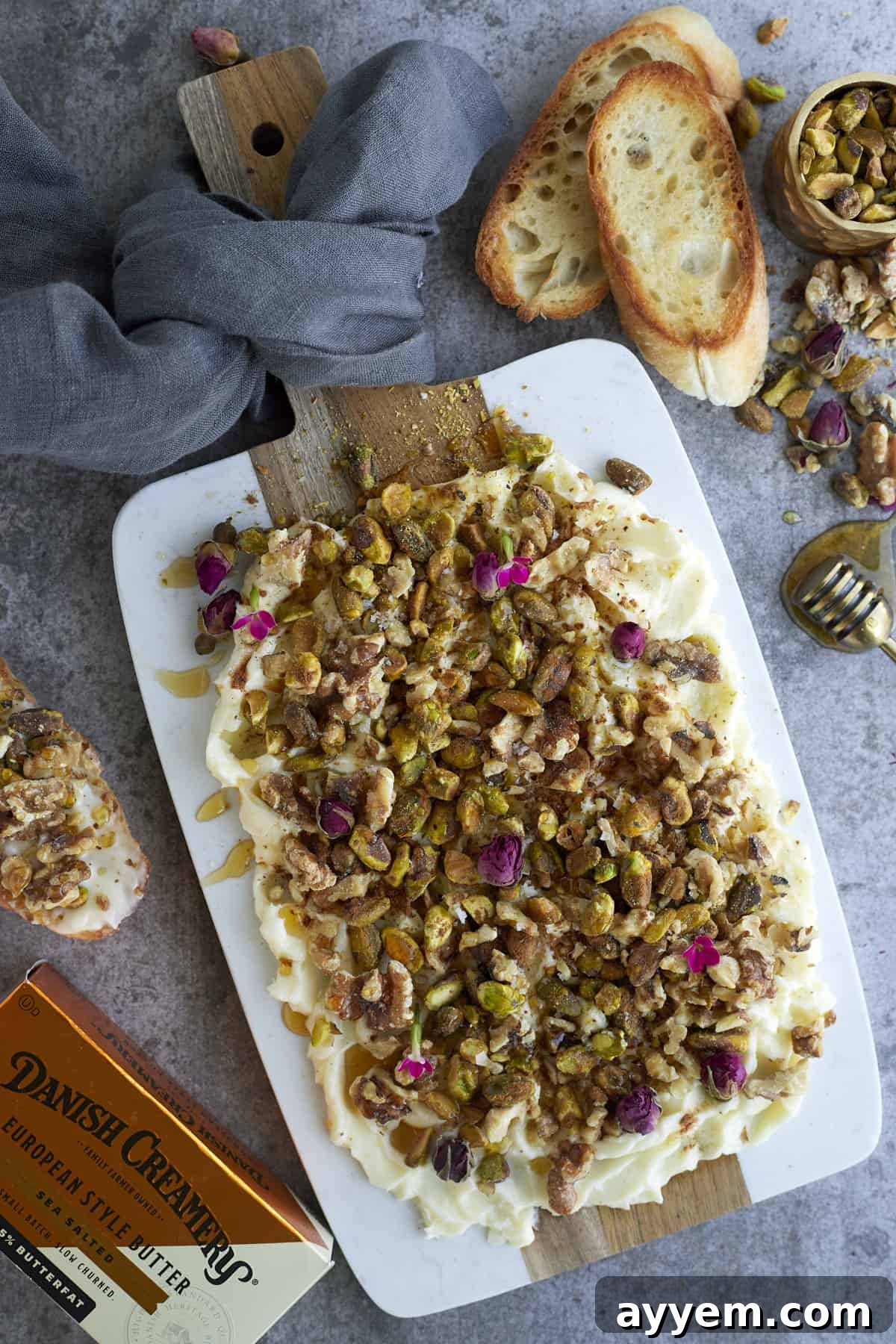 baklava butter on a white serving board surrounded by butter, crostini, and chopped nuts