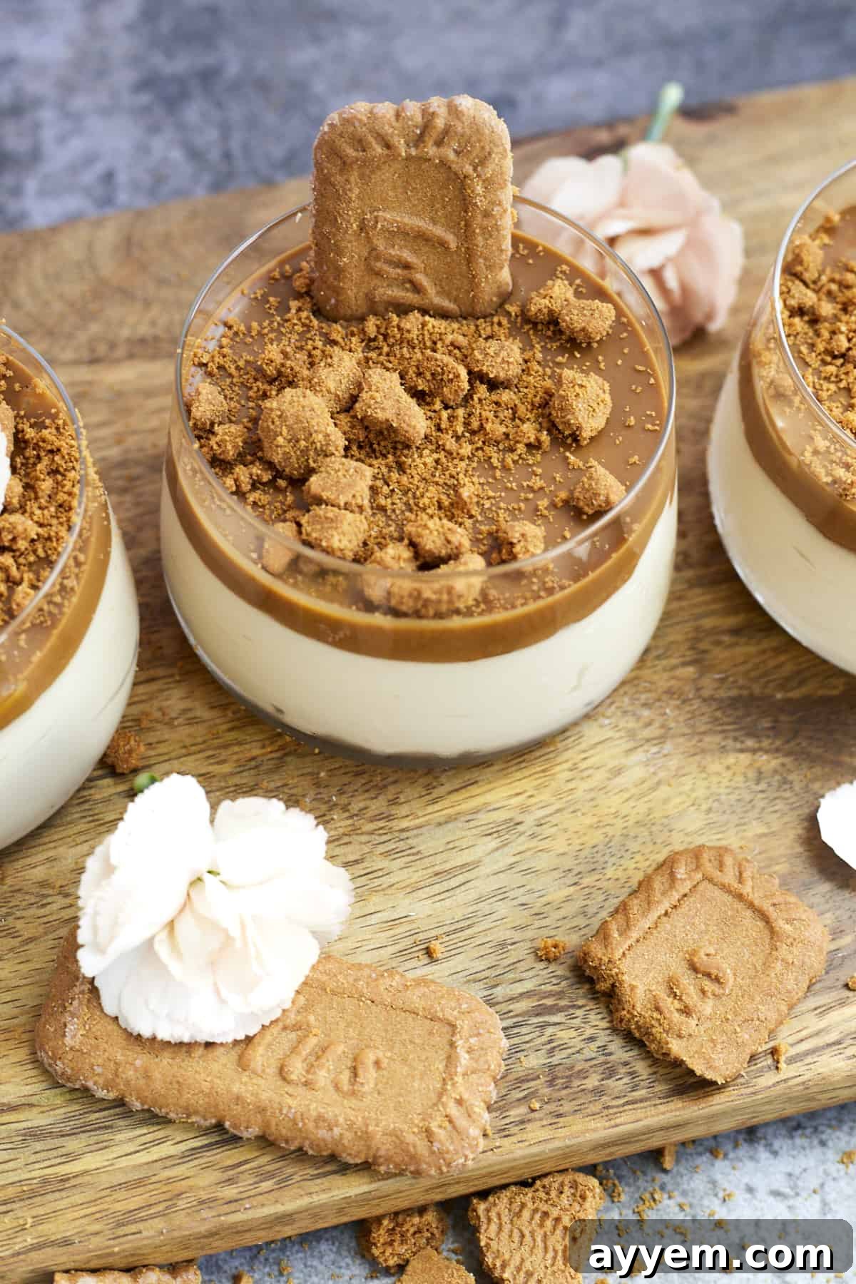 overehead image of jars of biscoff mousse topped with Biscoff spread and Biscoff cookies on a wooden board with Biscoff cookies scattered around
