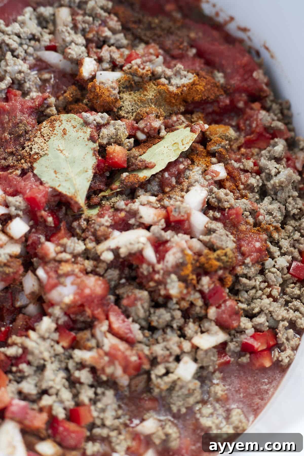 Close up image of a beef and bean mixture simmering in a slow cooker, indicating the initial stages of cooking for Middle Eastern Beef Chili.