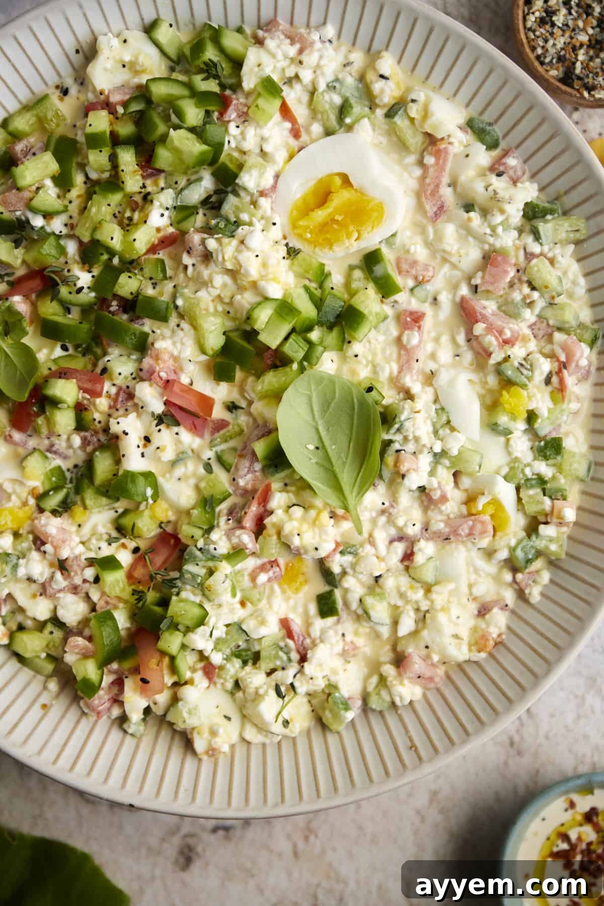 overhead image of the best egg salad recipe in a white bowl topped with fresh herbs and sliced boiled eggs, emphasizing its inviting texture