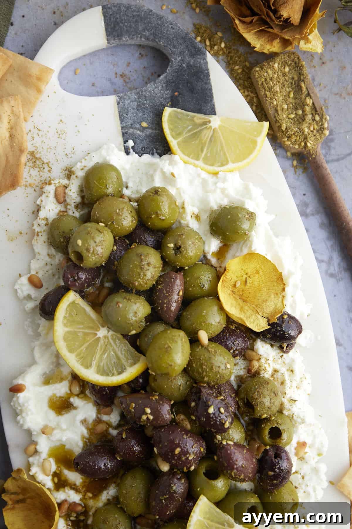 A beautifully arranged feta board topped with marinated olives, fresh herbs, and a drizzle of olive oil, ready to be served.