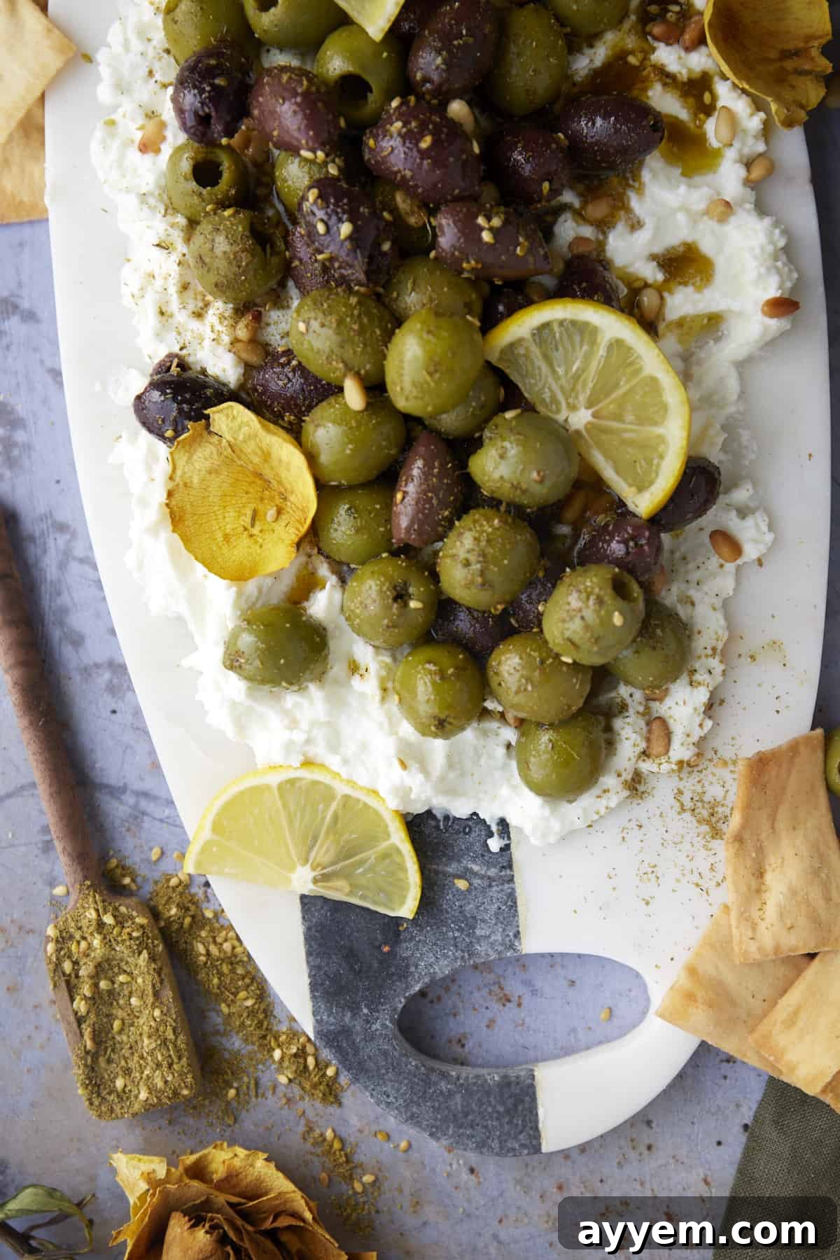 An overhead shot of a vibrant feta board adorned with marinated olives, fresh lemon wedges, and a sprinkle of aromatic spices, inviting a delightful tasting experience.