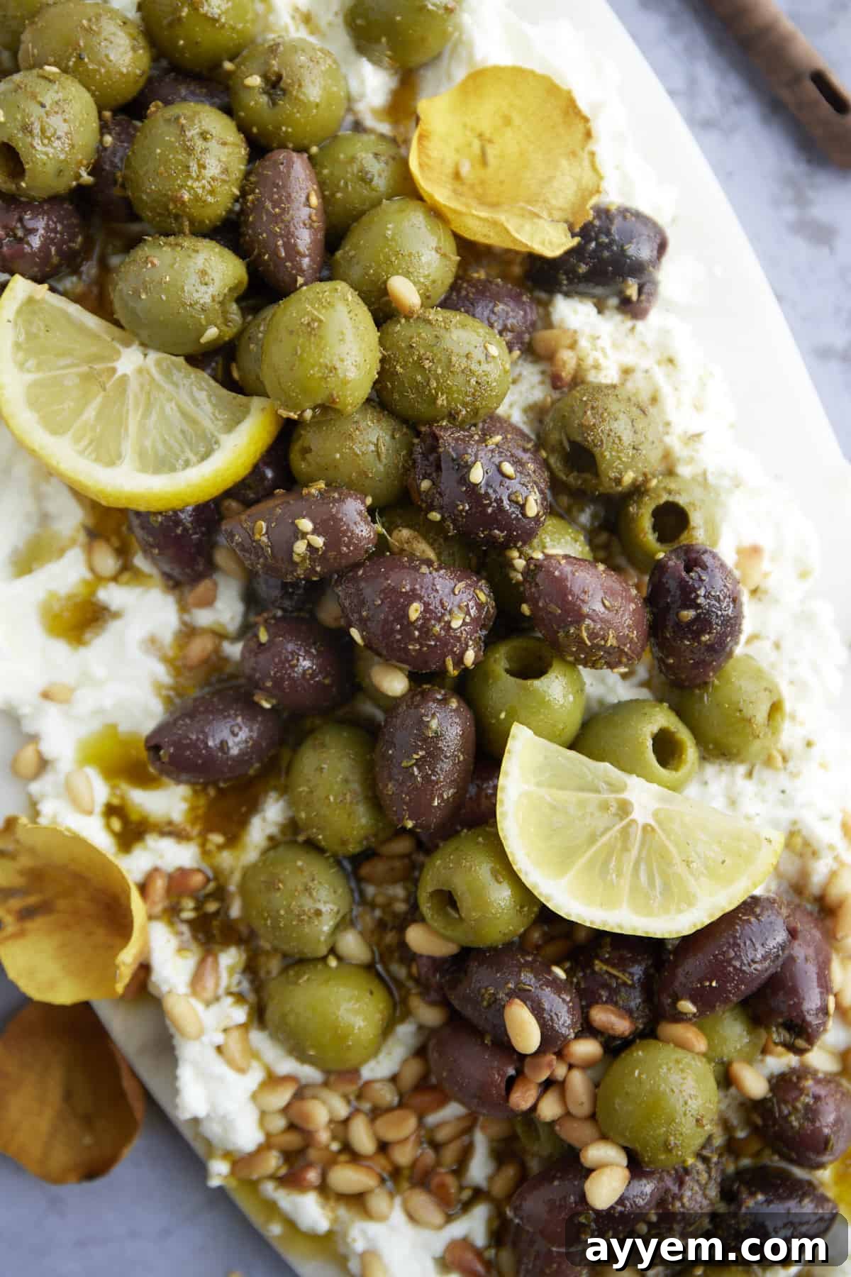 A close-up, tempting image of a feta board generously topped with a medley of marinated olives, showcasing the creamy texture of the feta and the vibrant colors of the toppings.