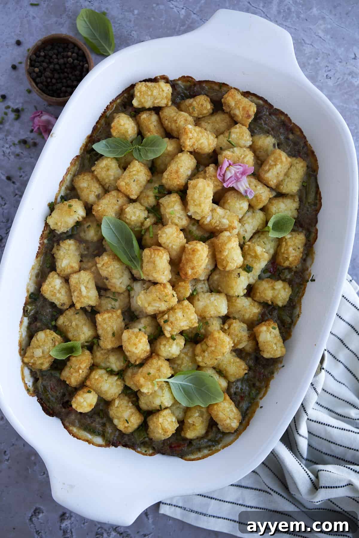 Tater tot hotdish in a white casserole dish, topped with fresh herbs, ready to be served