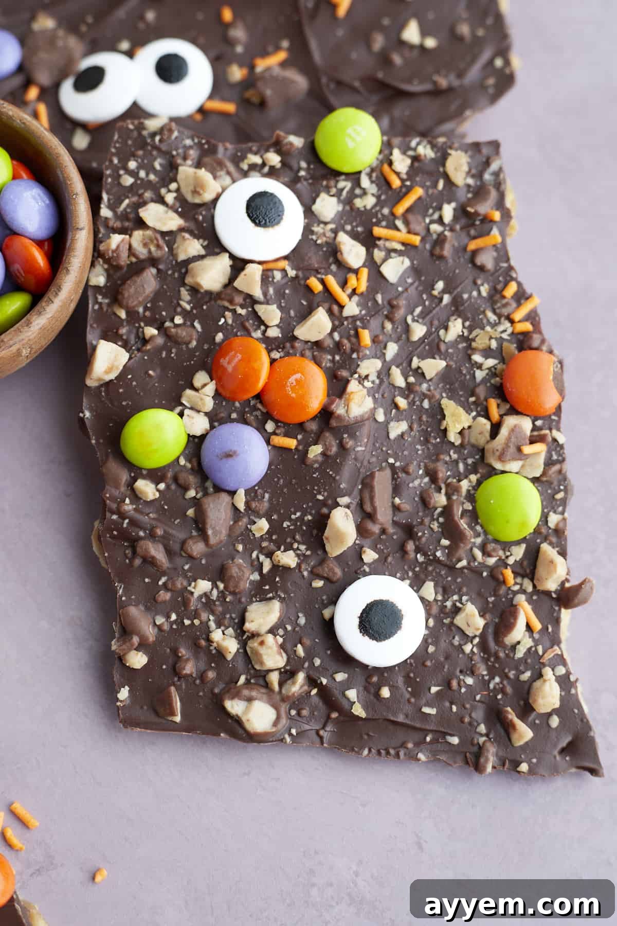 close up image of a piece of Halloween saltine crack candy topped with toffee bits, candy eyeballs, orange sprinkles, and M&Ms