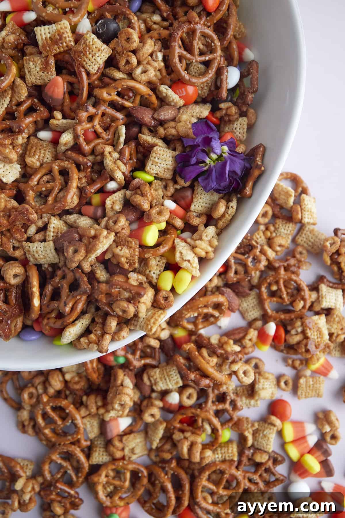 a white bowl full of Halloween snack mix with more mix scattered on a table around it 