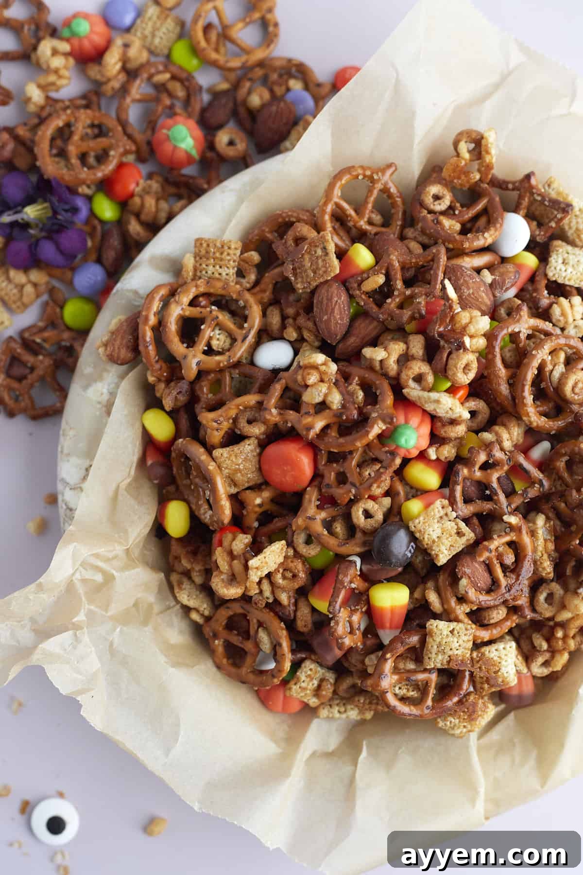a parchment paper-lined bowl of Halloween snack mix with more snack mix on the table next to it