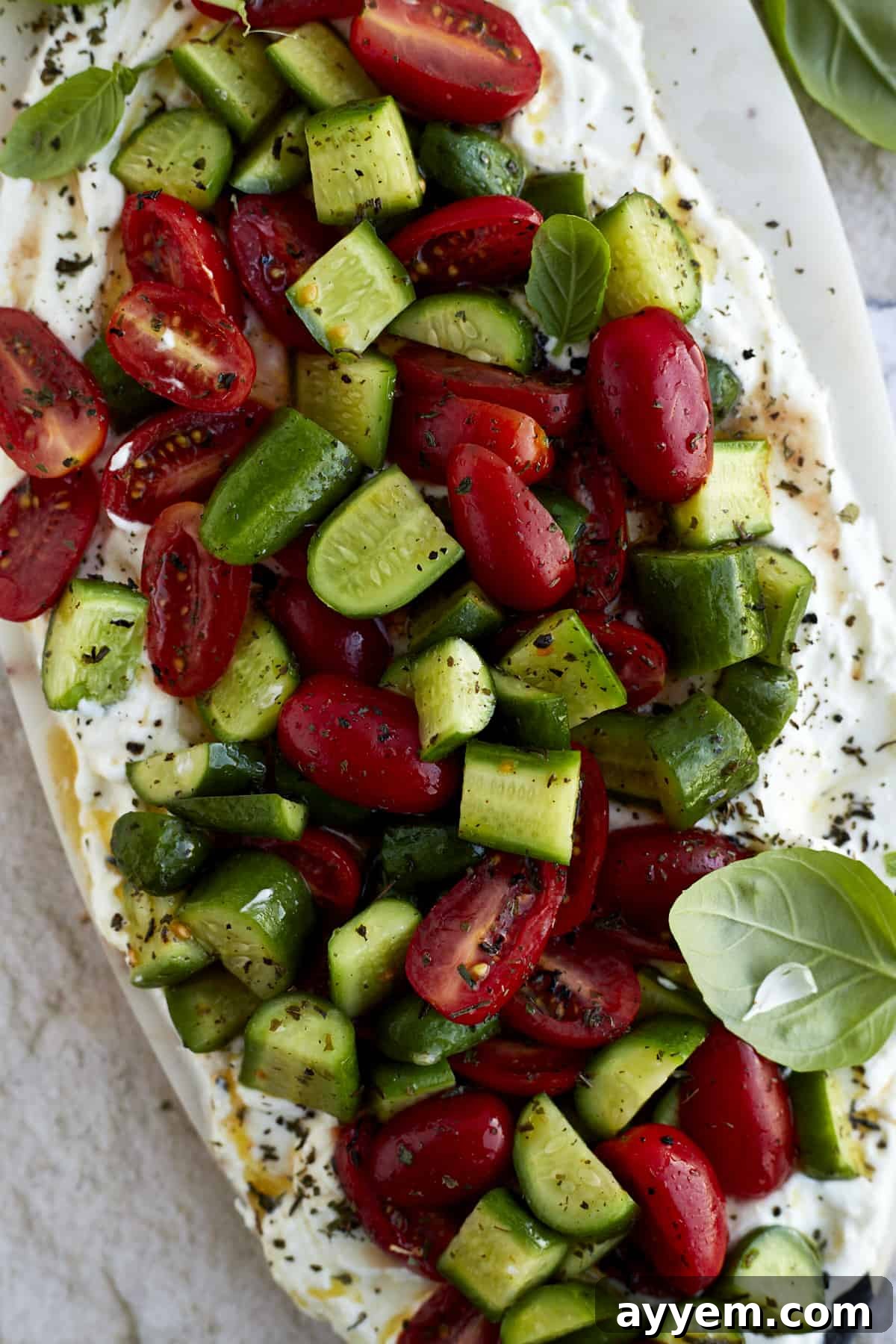 Close-up shot of the creamy whipped feta base, dotted with colorful cherry tomatoes and cucumber slices, garnished with fresh herbs, ready to be served.