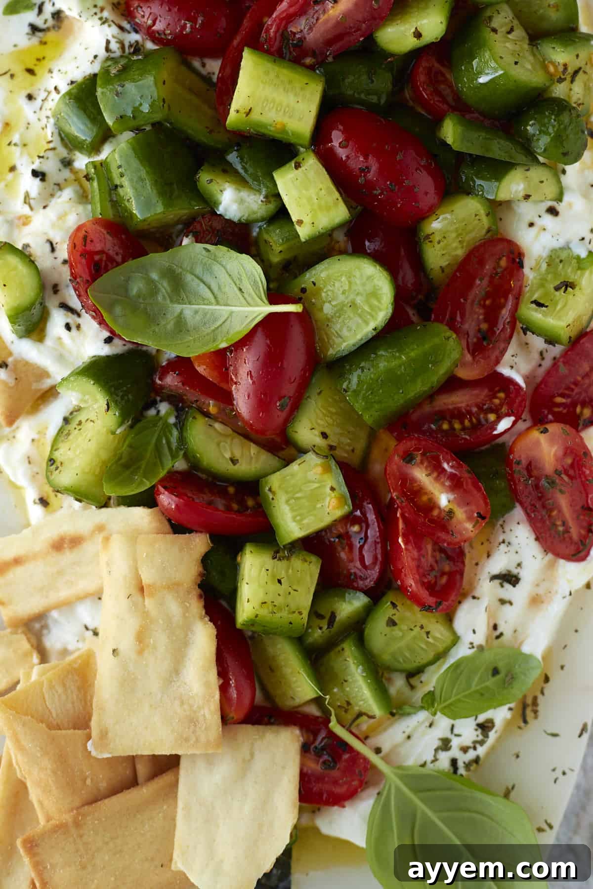 Overhead view of the finished cucumber and tomato salad with whipped feta, artfully arranged on a serving board with a generous layer of creamy feta underneath and fresh herbs as garnish.