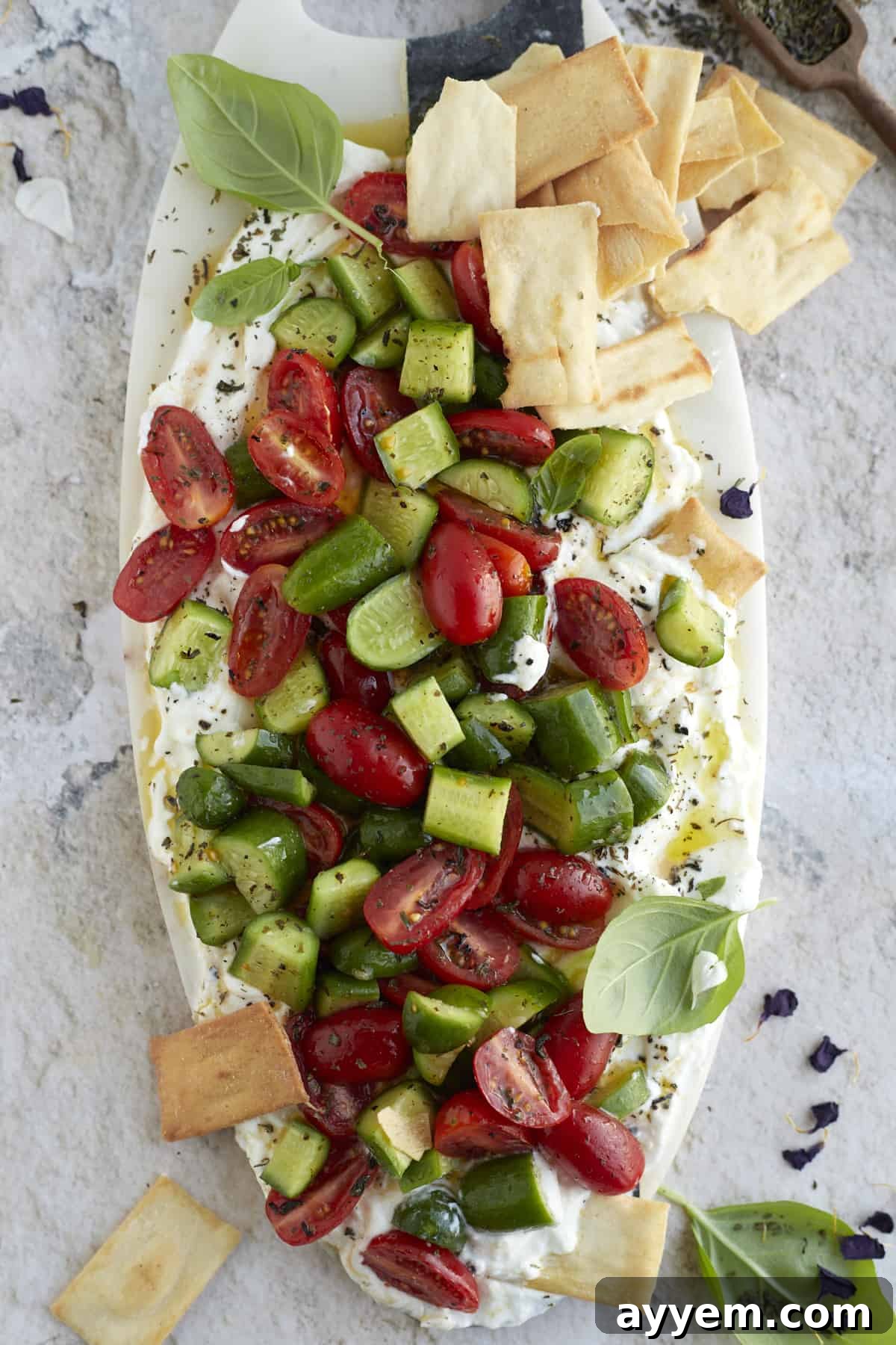 overhead image of cucumber and tomato salad layered over whipped feta dip with pita chips on the side