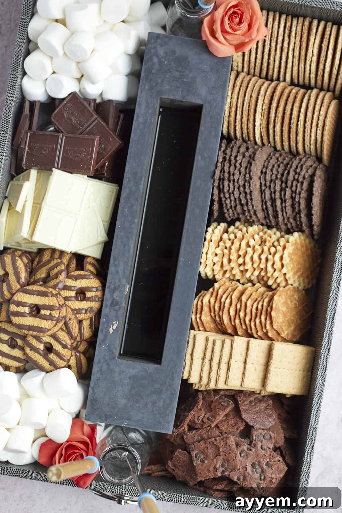 A close-up view of a bustling indoor s'mores board, showcasing a portable tabletop fire pit casting a warm glow over an assortment of gourmet cookies, plump marshmallows, various chocolate bars, and crisp graham crackers, ready for roasting.
