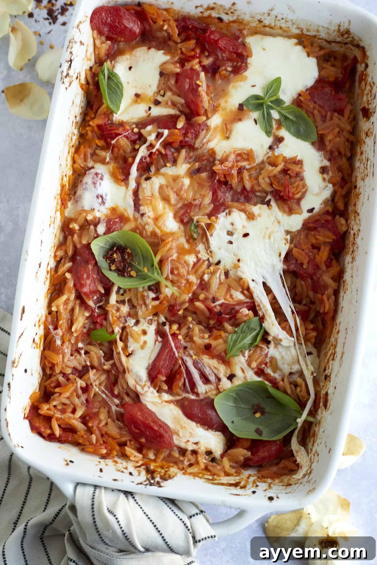 Overhead image of caprese baked orzo pasta in a casserole dish with melted mozzarella on top, garnished with fresh basil.