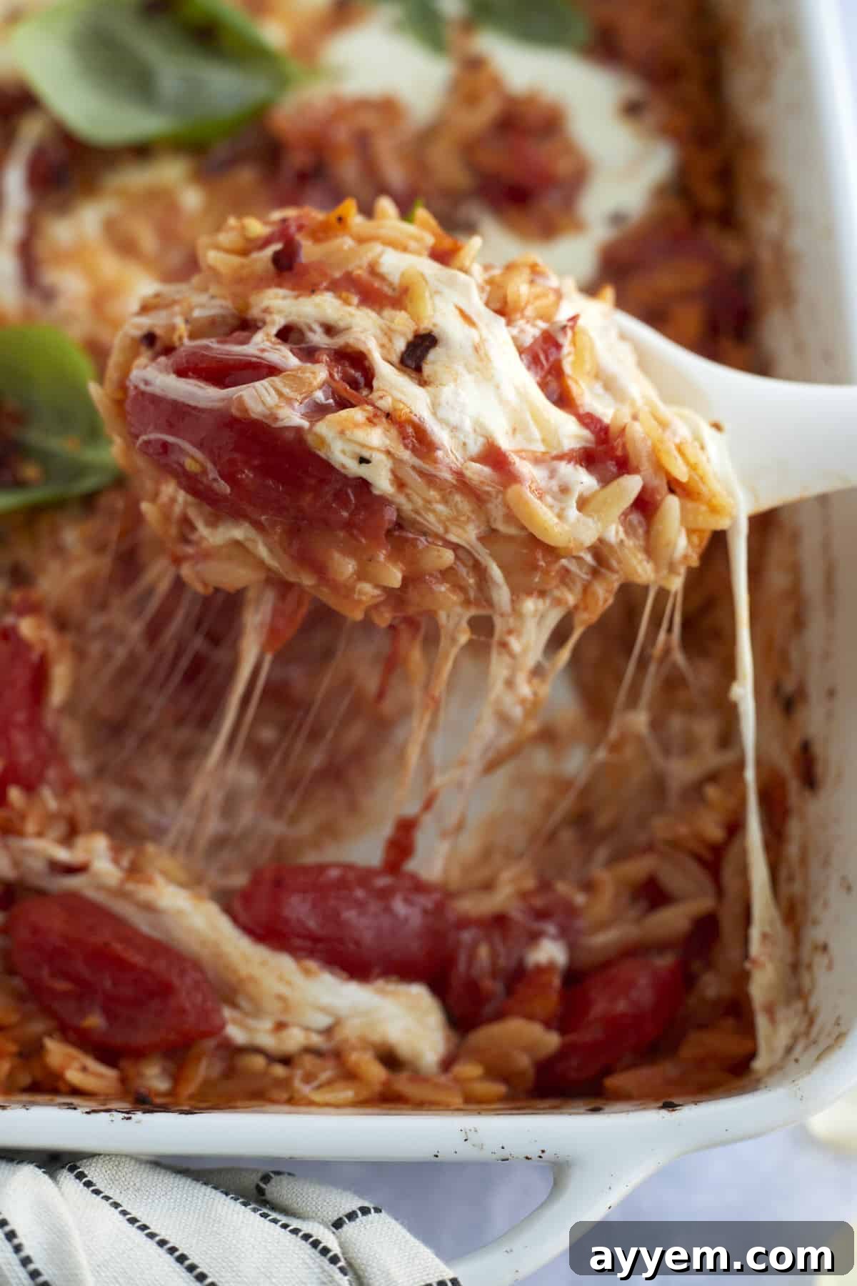 A serving of Caprese baked orzo pasta being lifted from a casserole dish, showing the cheesy, tomato-rich pasta.