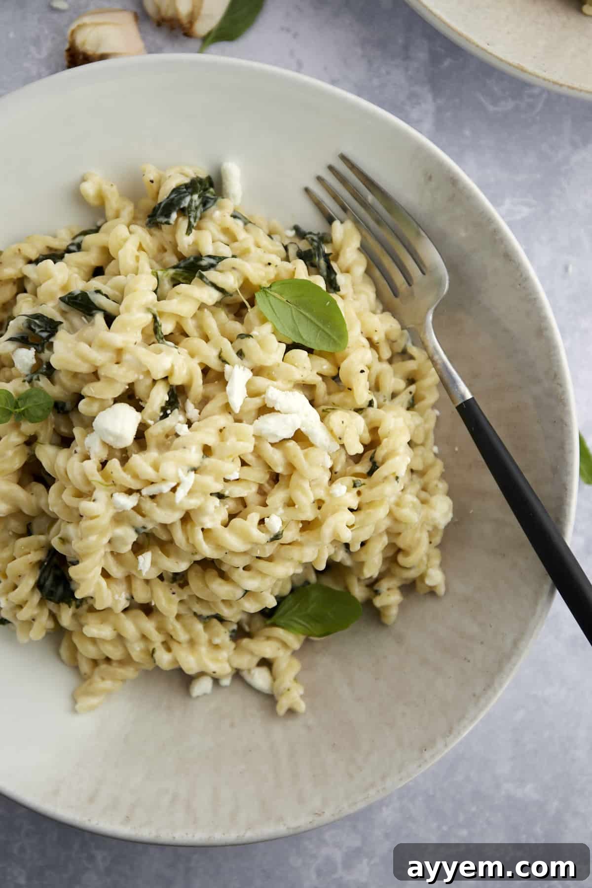 A beautifully presented white bowl of creamy Spanakopita Pasta with Spinach, with a fork resting beside it.