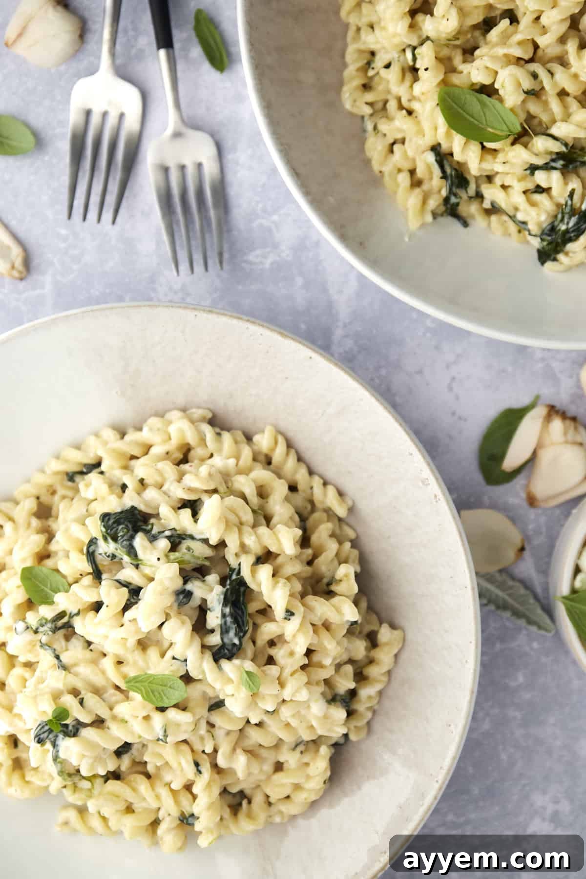 Two enticing bowls of creamy Spanakopita Pasta with Spinach, garnished, with forks ready for dining.