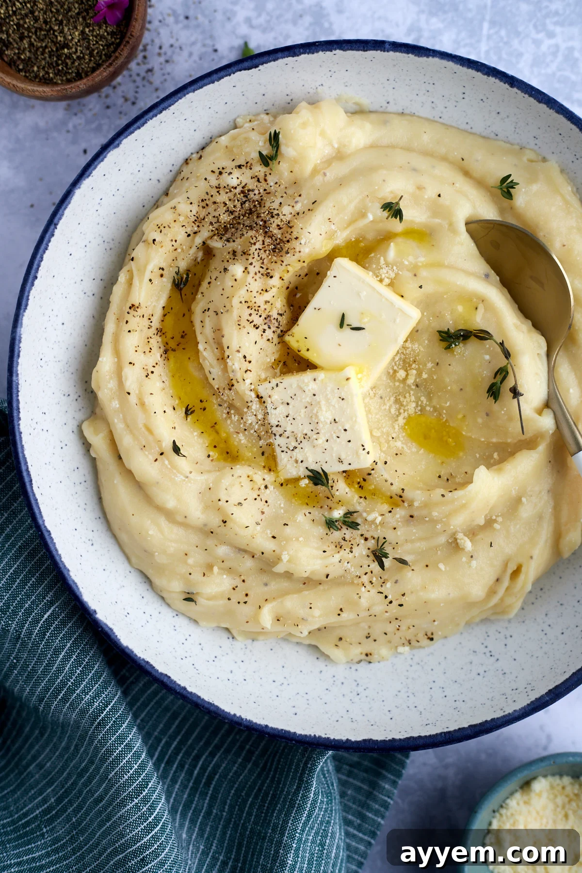 A large bowl of creamy slow cooker mashed potatoes, garnished with melting butter pads and a sprinkle of fresh herbs.
