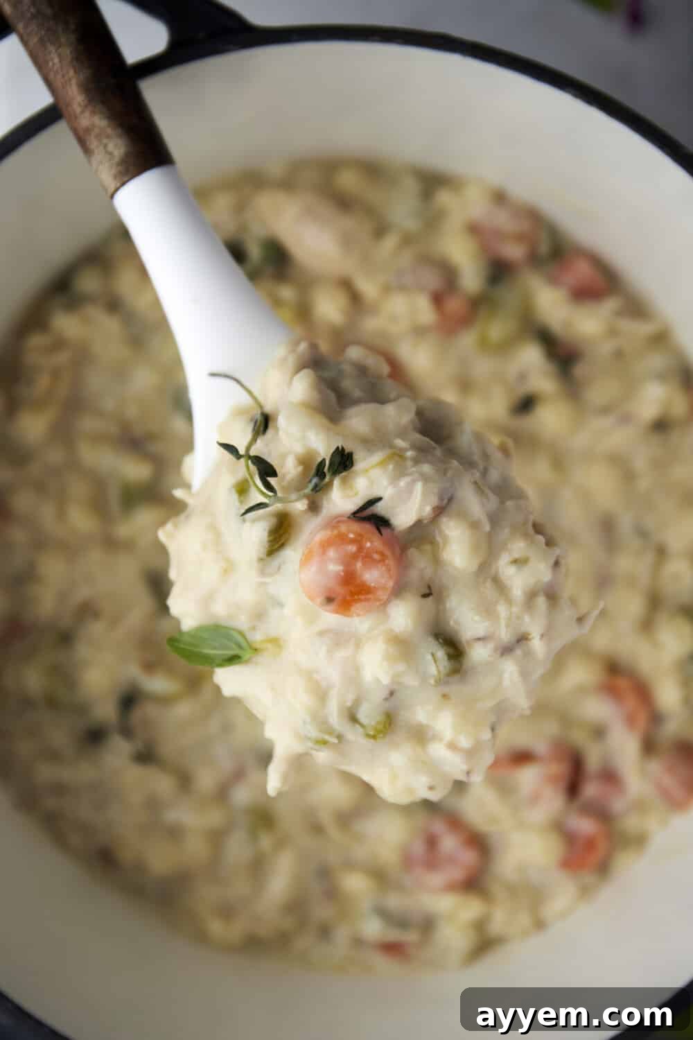 A close-up of a spoonful of creamy chicken noodle soup being lifted from a steaming bowl, showing the perfectly cooked noodles and tender chicken.