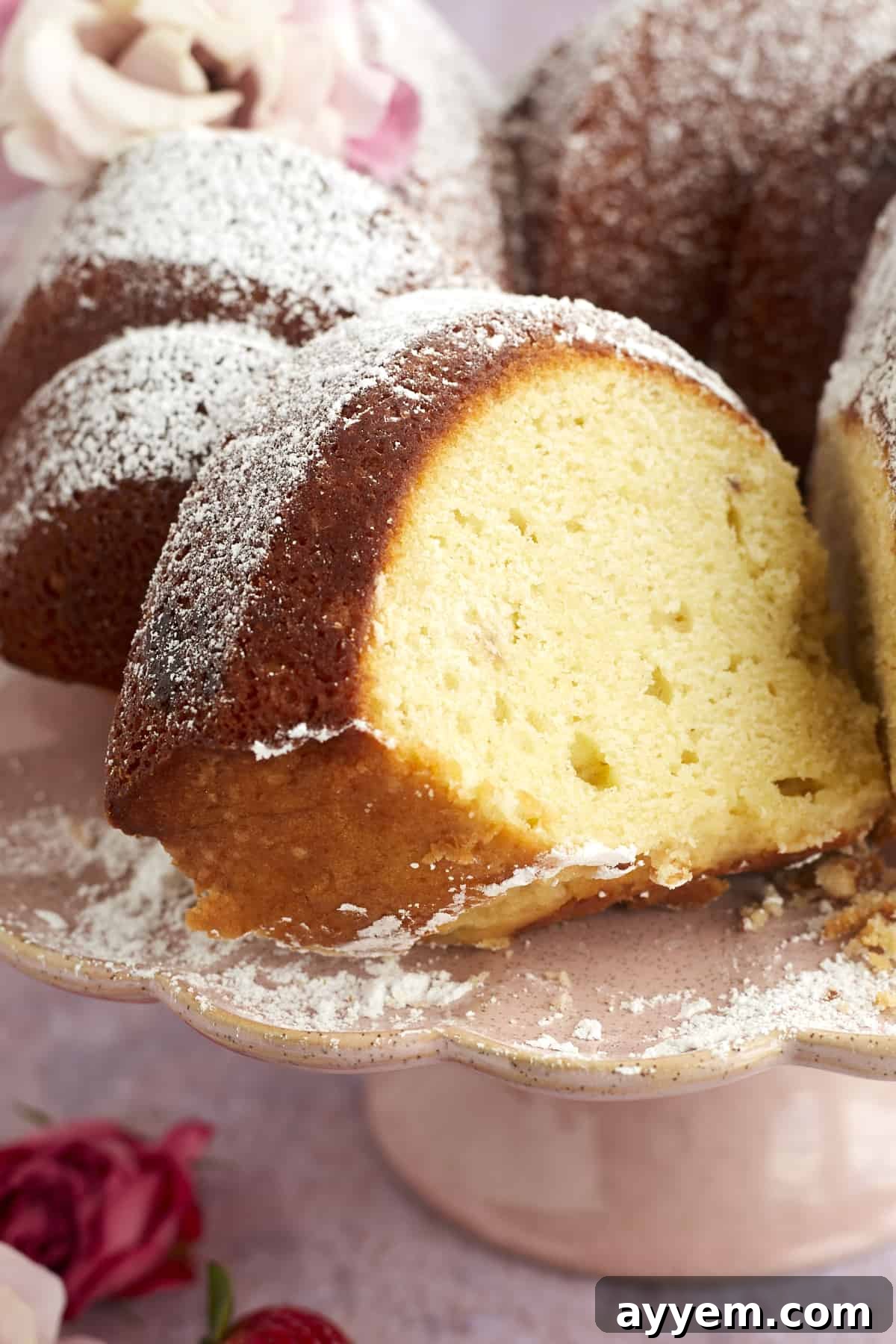 A close-up shot of a perfect slice of strawberry lemon bundt cake, elegantly dusted with powdered sugar and resting on a white plate.