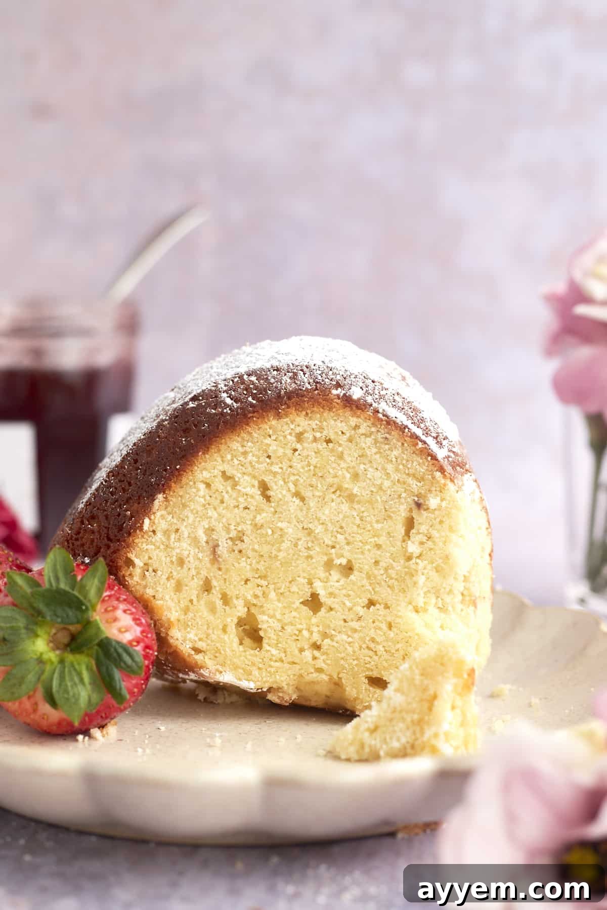 A side view of a slice of bundt cake, adorned with powdered sugar, served on a plate alongside whole fresh strawberries.