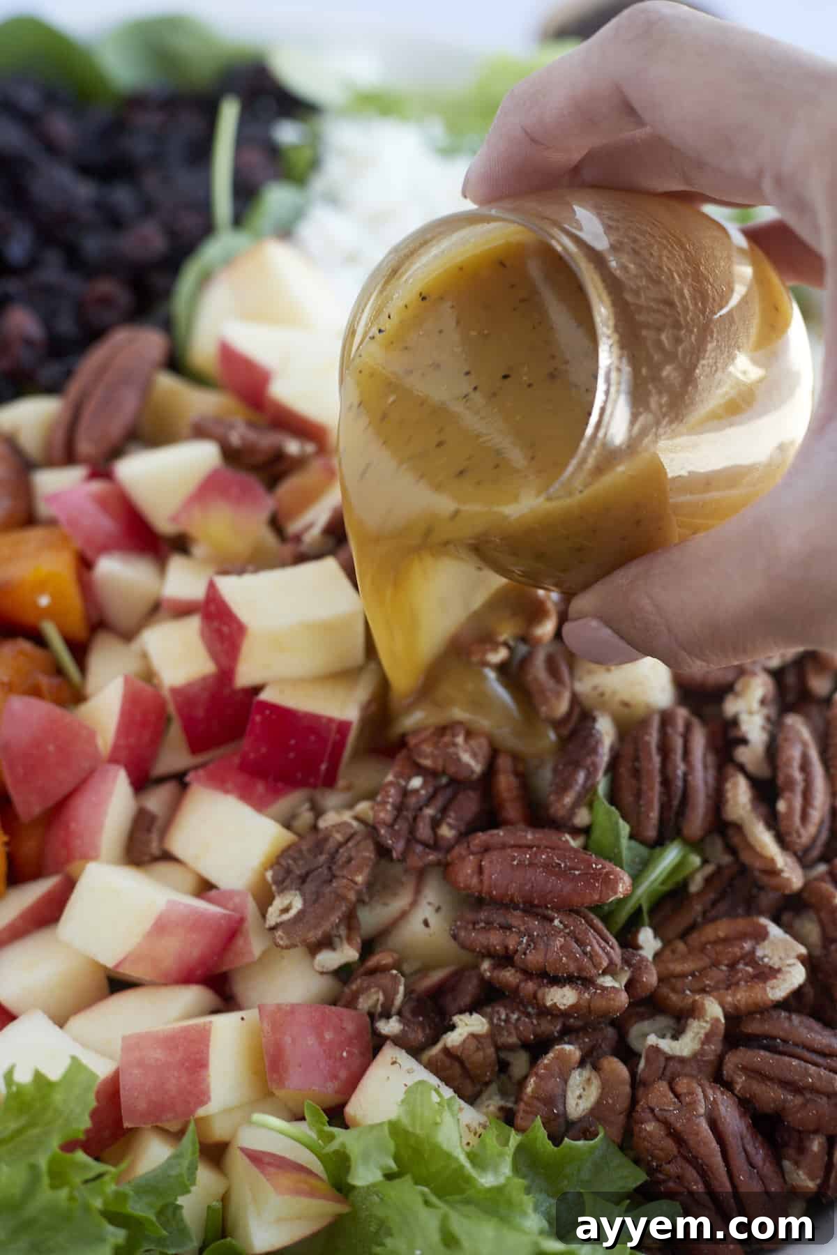 a hand drizzling dijon salad dressing over roasted butternut squash salad